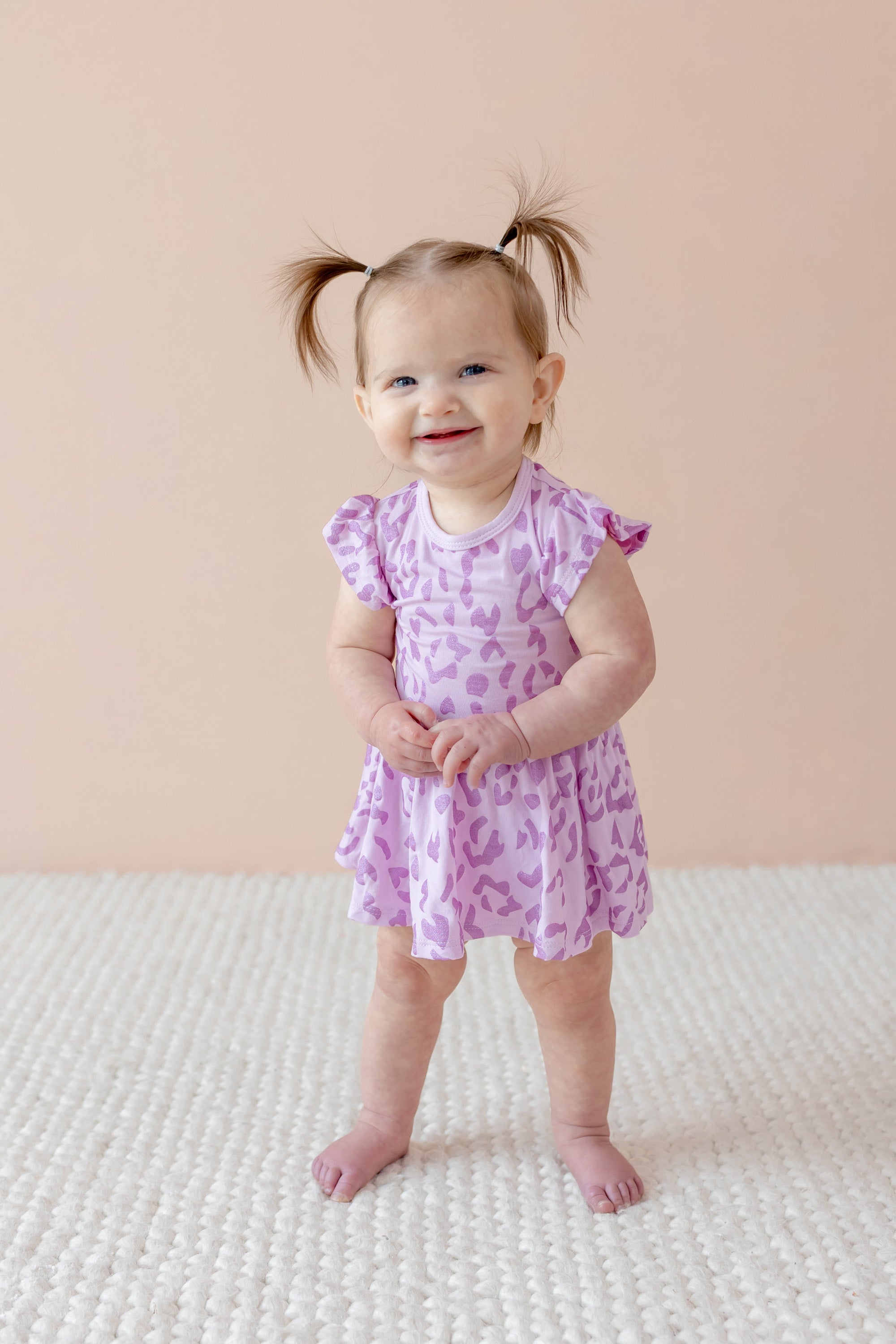 Child posing in Twirl bodysuit dress in Thistle Leopard print on a beige background