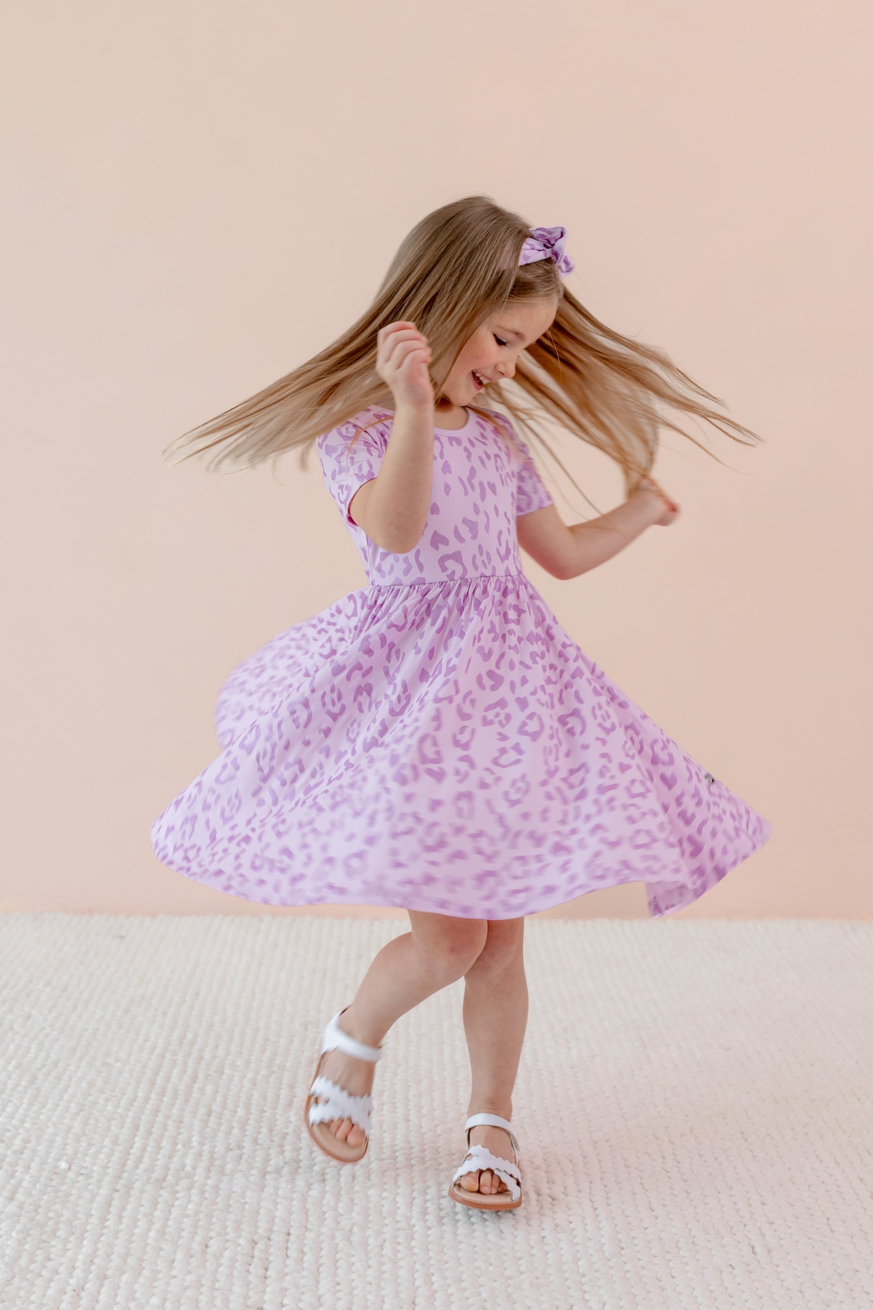 Child twirling in Thistle Leopard print Twirl Dress wearing a similar print bow headband and white sandles on a beige background