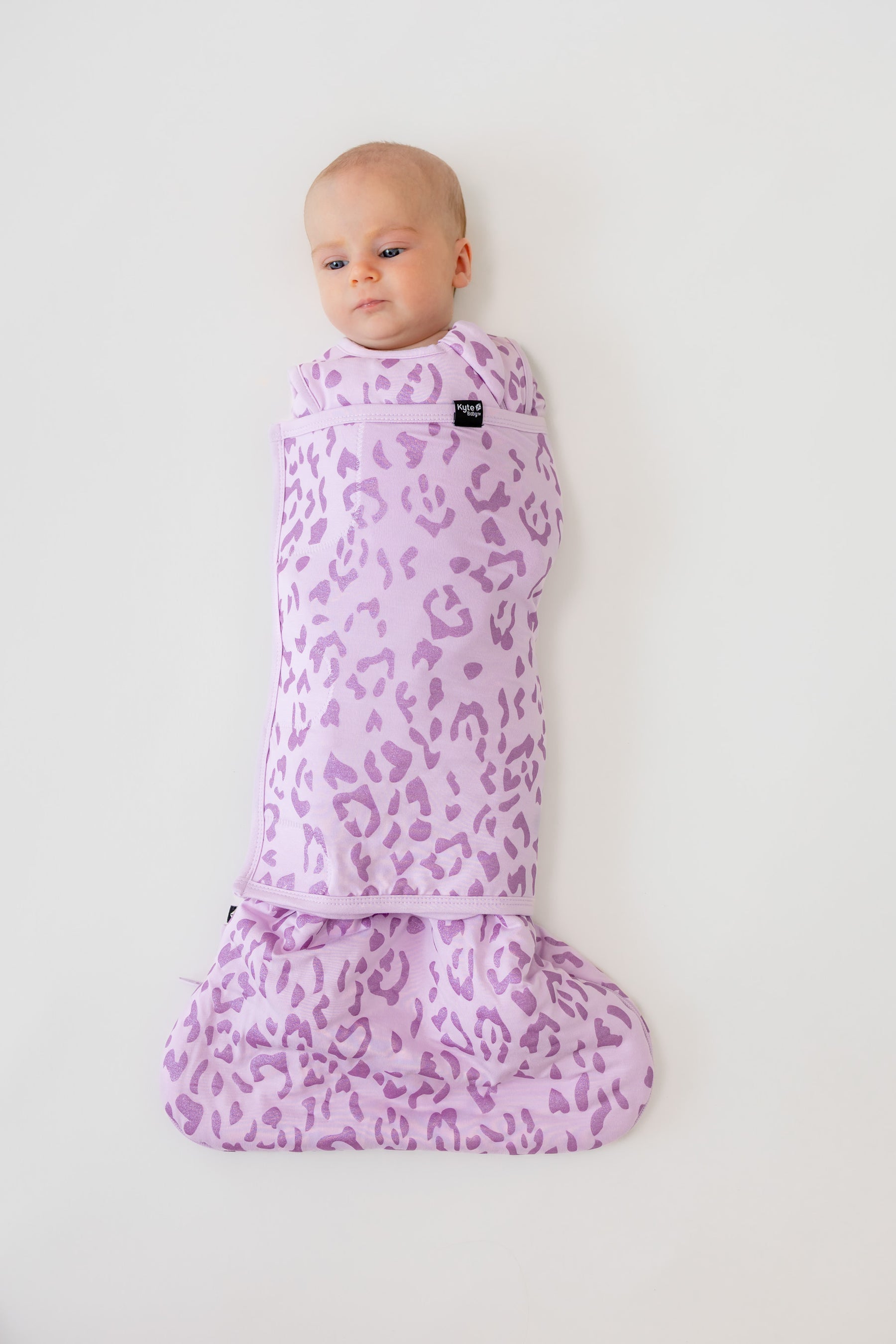 Baby in Thistle Leopard print sleep bag swaddler on a white background