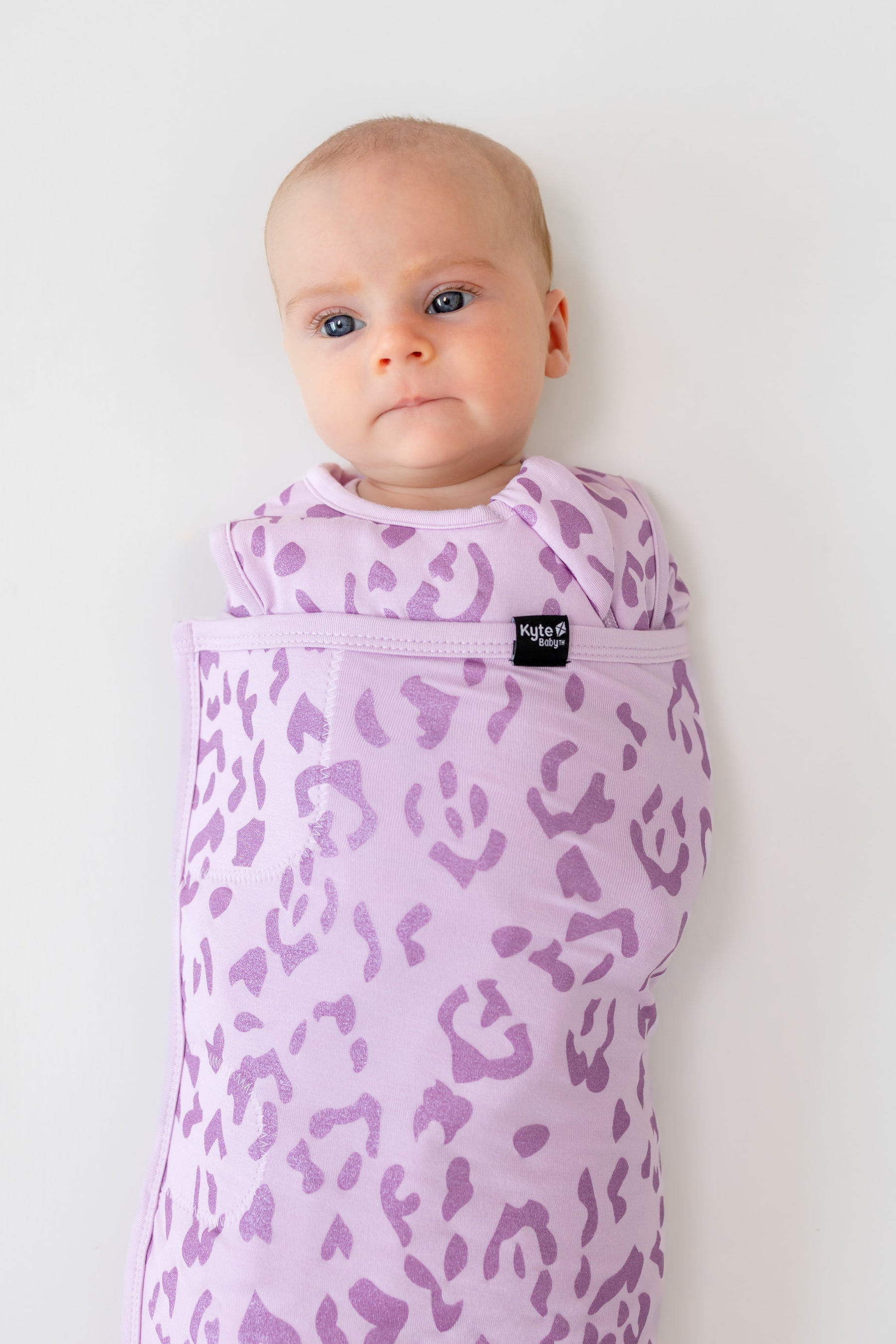 Baby in sleep bag swaddler with Thistle Leopard print on a white background