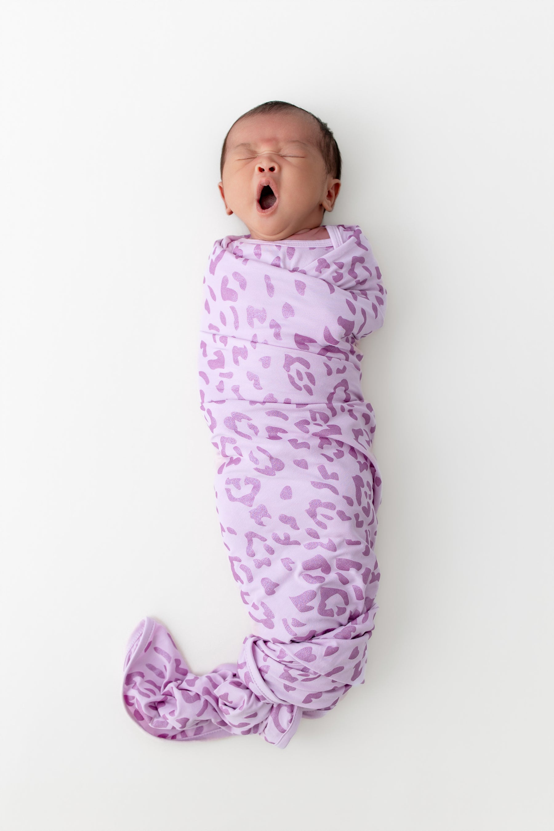 Baby yawning in a Thistle Leopard print Swaddle blanket on a white background
