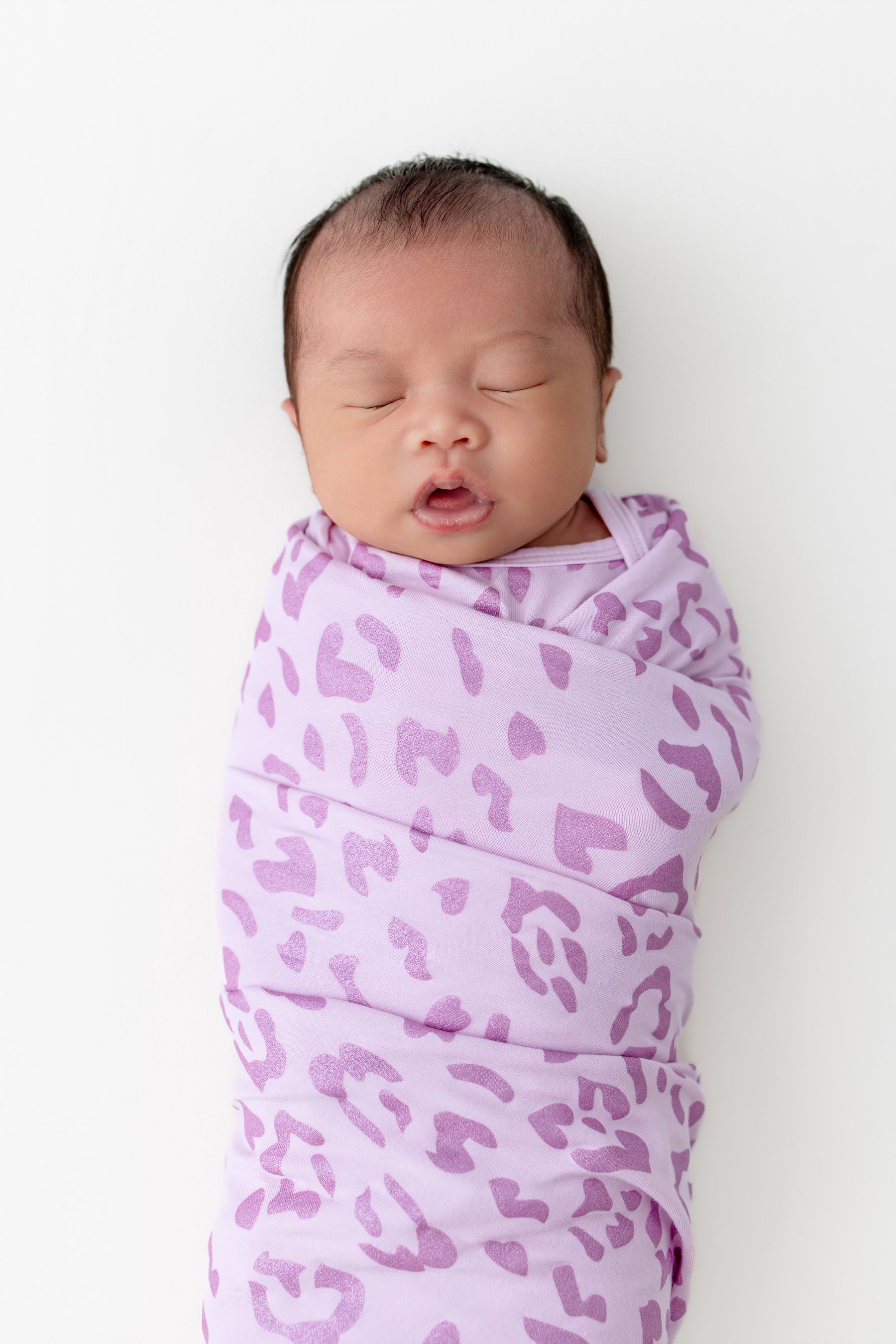 Baby sleeping in a Swaddle blanket with Thistle Leopard print on a white background