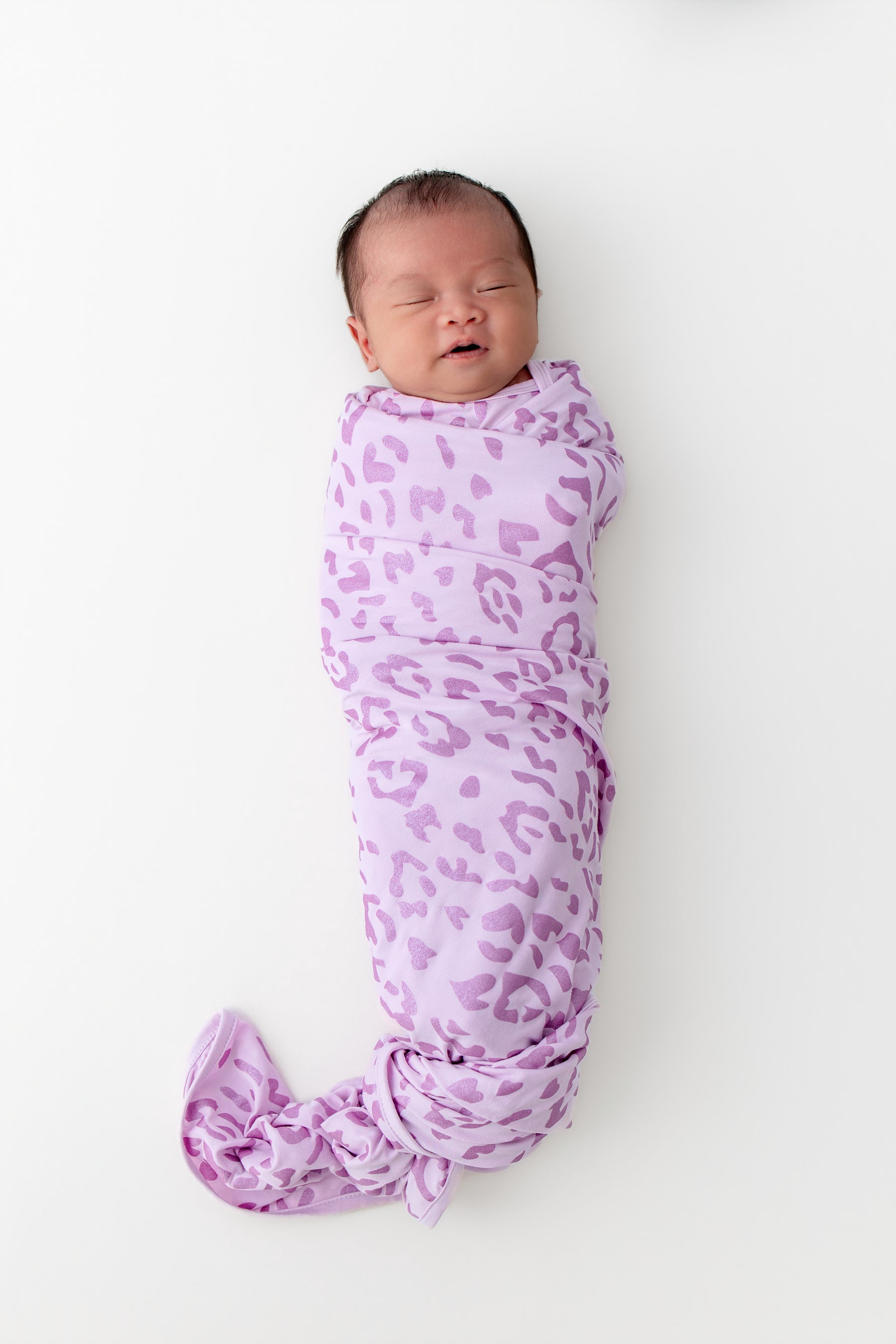 Baby sleeping in a Swaddle blanket with Thistle Leopard print on a white background