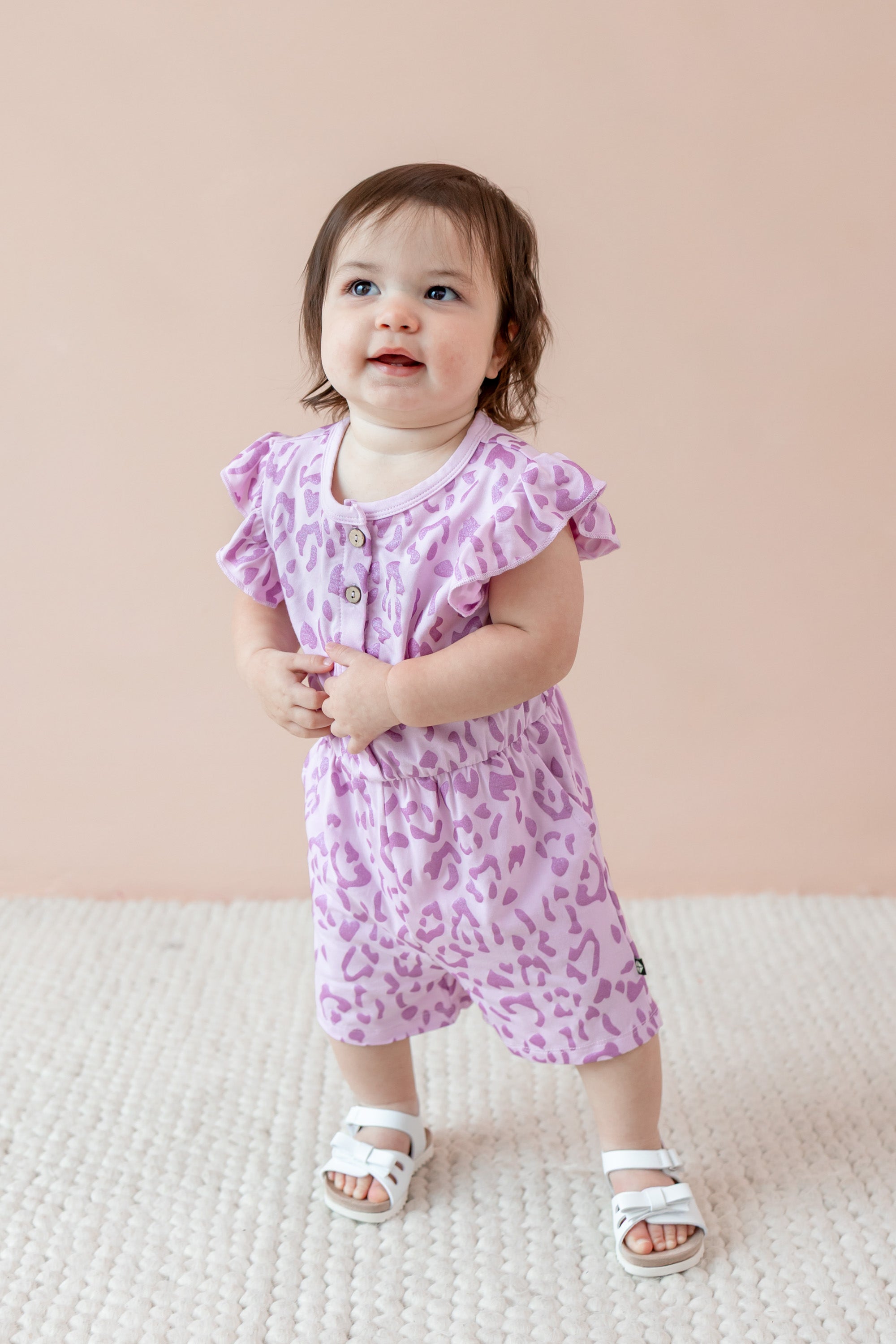 Child wearing a Thistle Leopard print Flutter Sleeve Romper with white sandles on a beige background