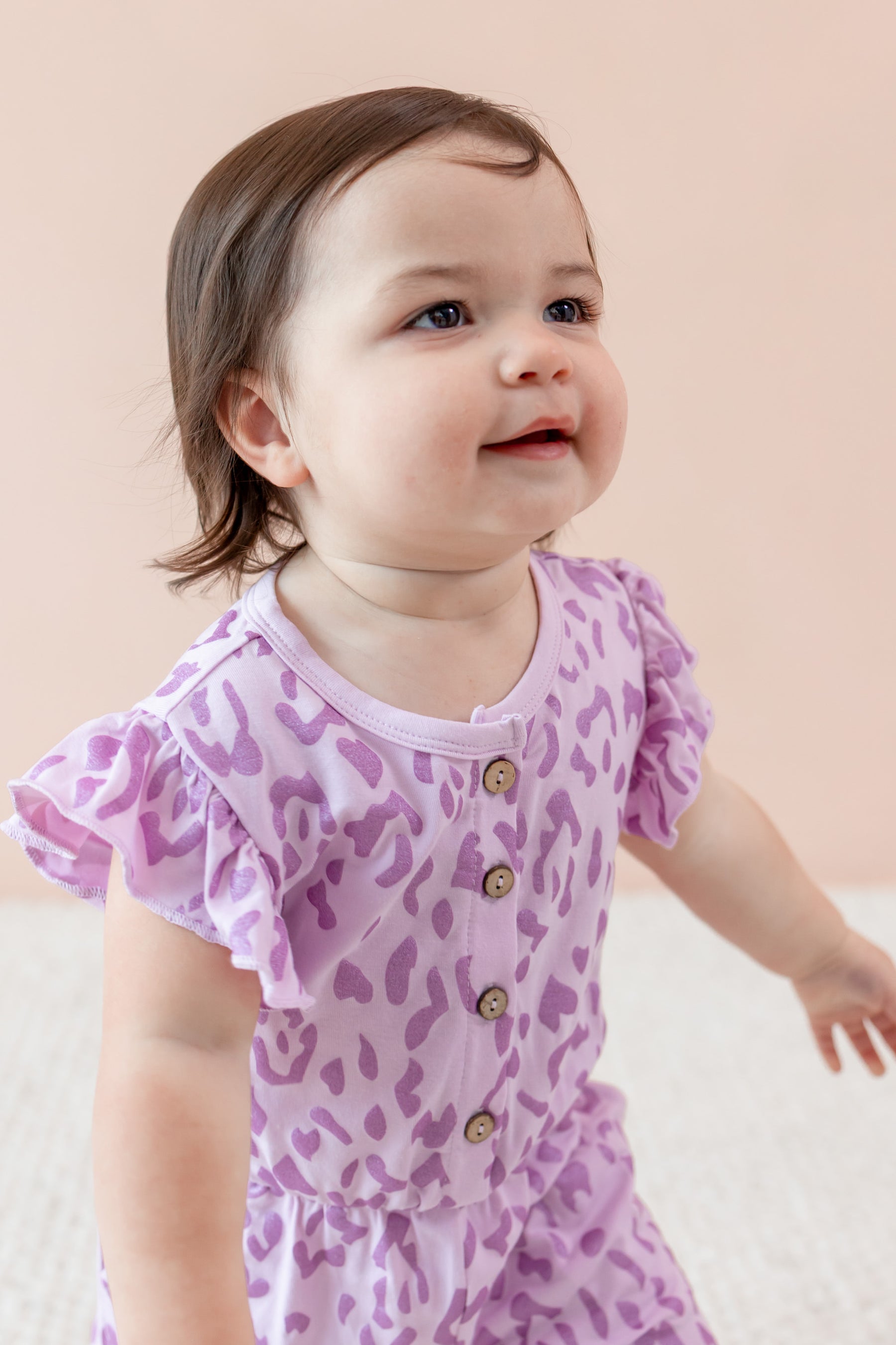 Child wearing a Thistle Leopard print Flutter Sleeve Romper on a beige background