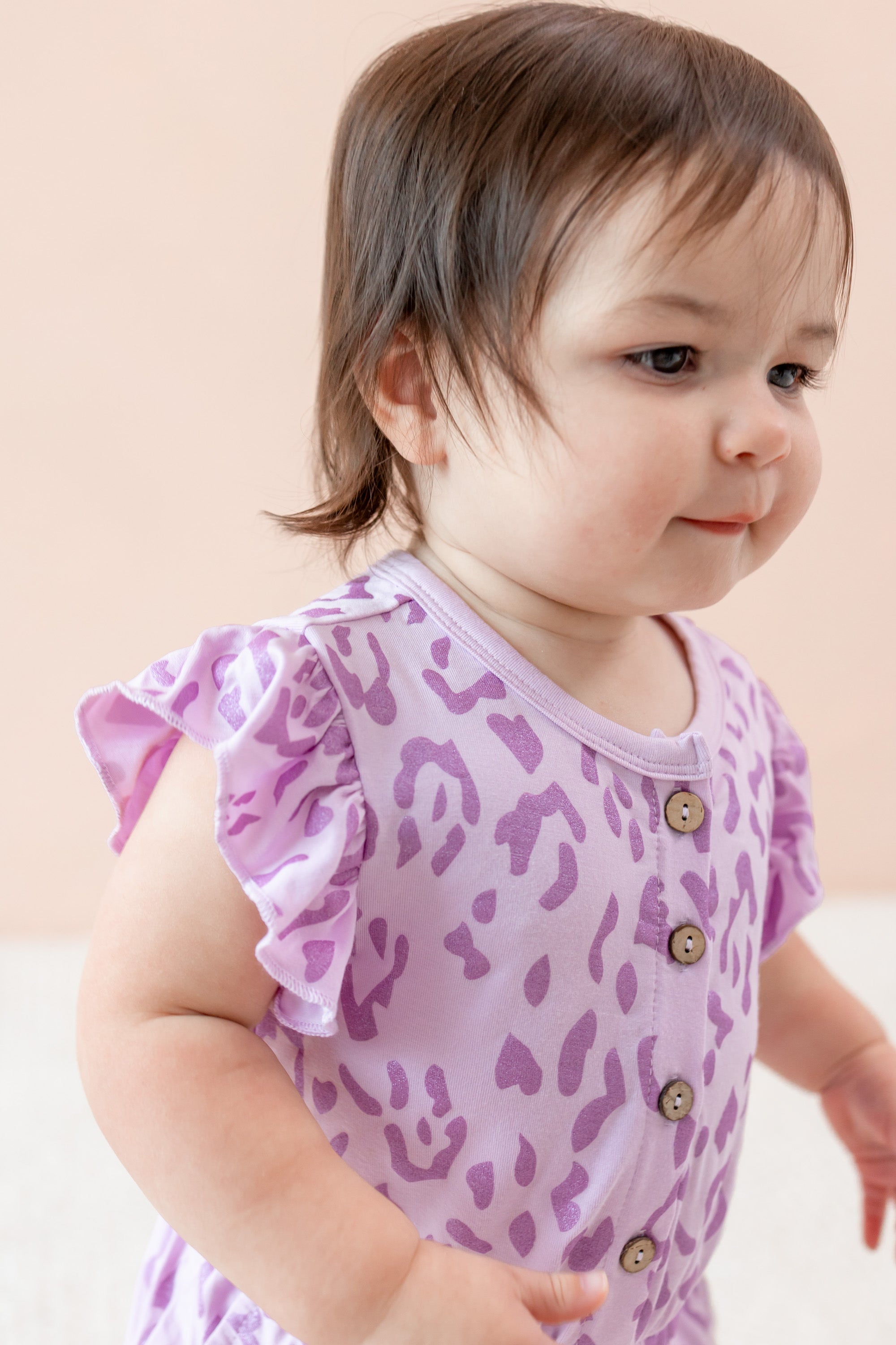 Child wearing a Thistle Leopard print Flutter Sleeve Romper on a beige background