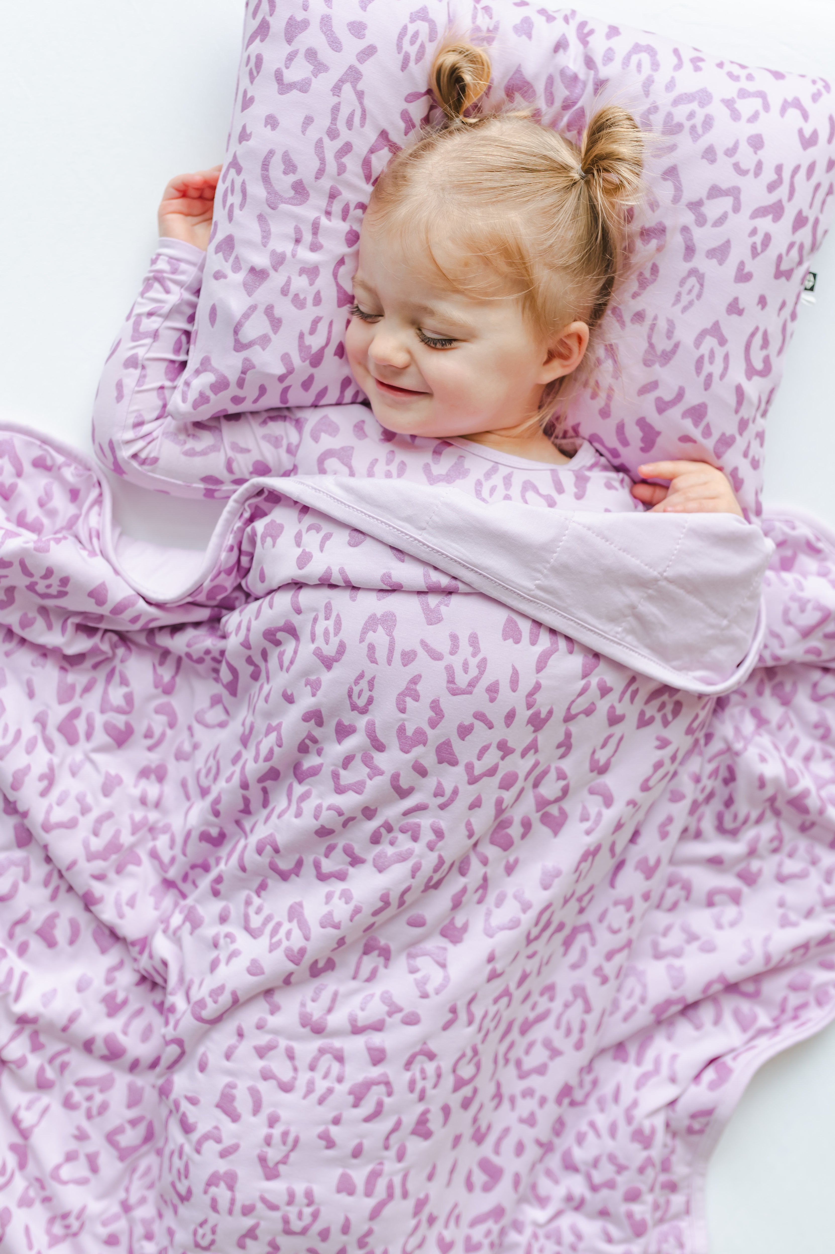 Child lying on a Thistle Leopard print  Toddler Pillowcase with a toddler blanket, wearing a similar print shirt on a white sheet