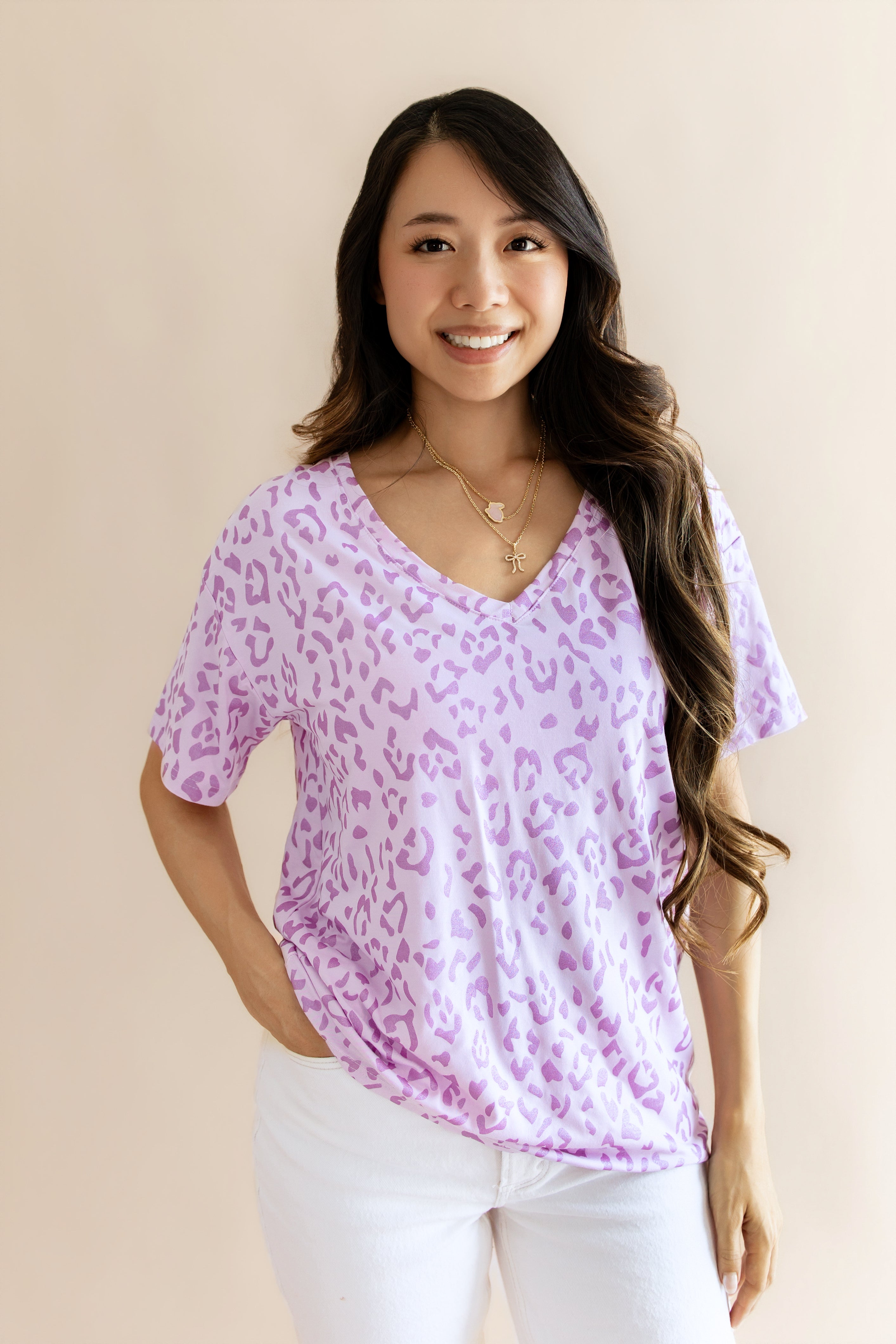 Model wearing Women's Relaxed Fit V-Neck in Thistle Leopard print over a white pant on a beige background