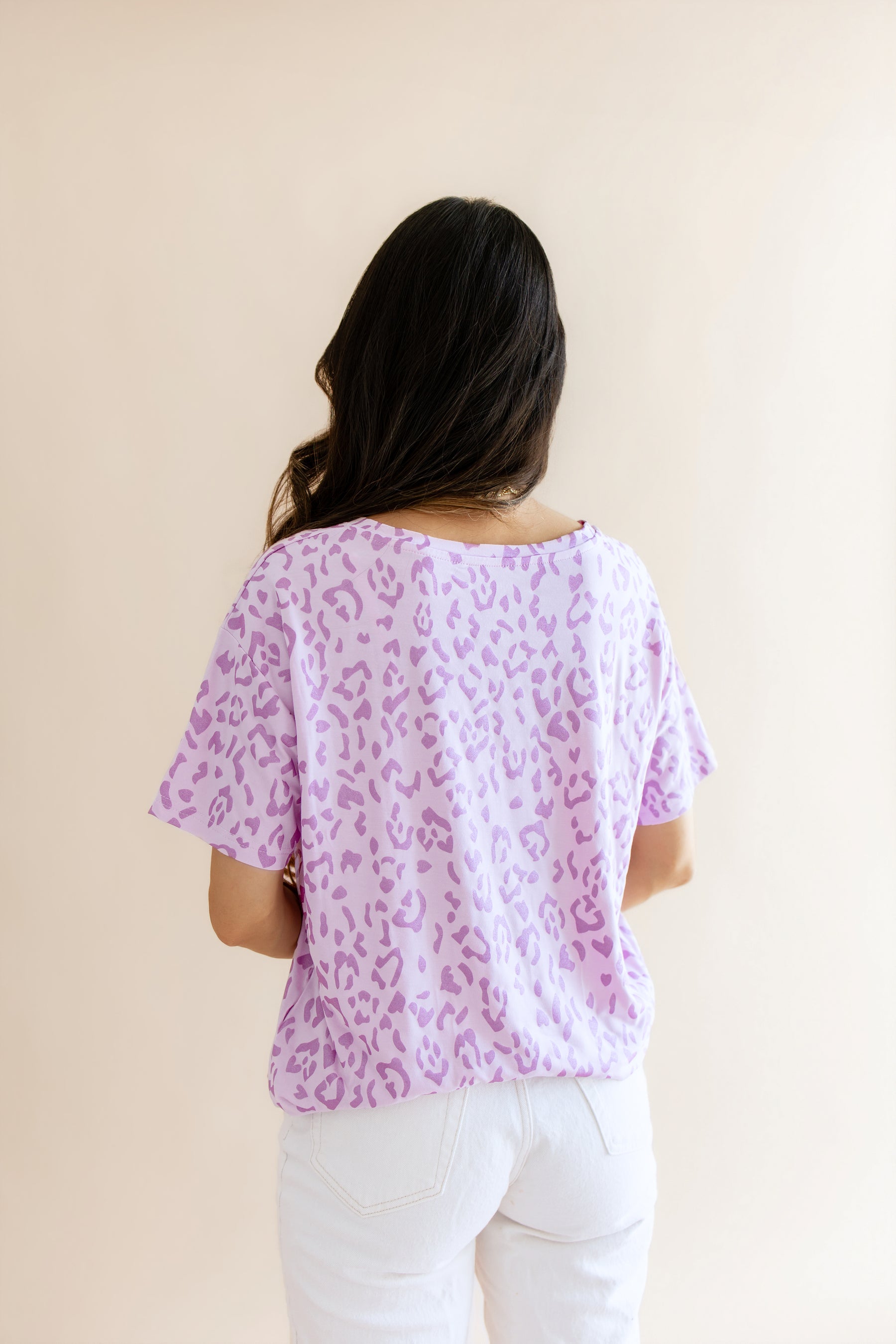 Back side of Women's Relaxed Fit V-Neck in Thistle Leopard print over a white pant on a beige background