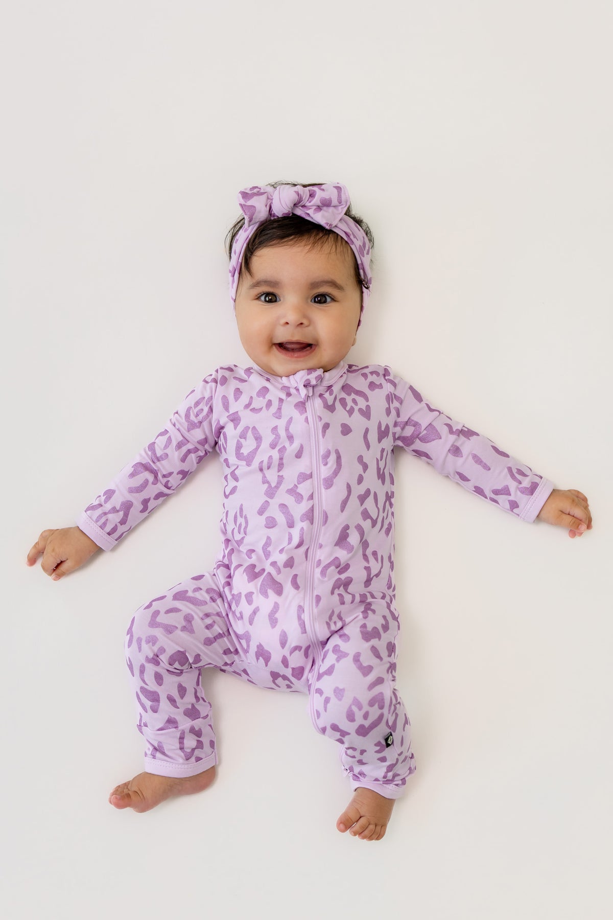 Baby wearing Thistle Leopard print zippered romper and bow headband on a beige background