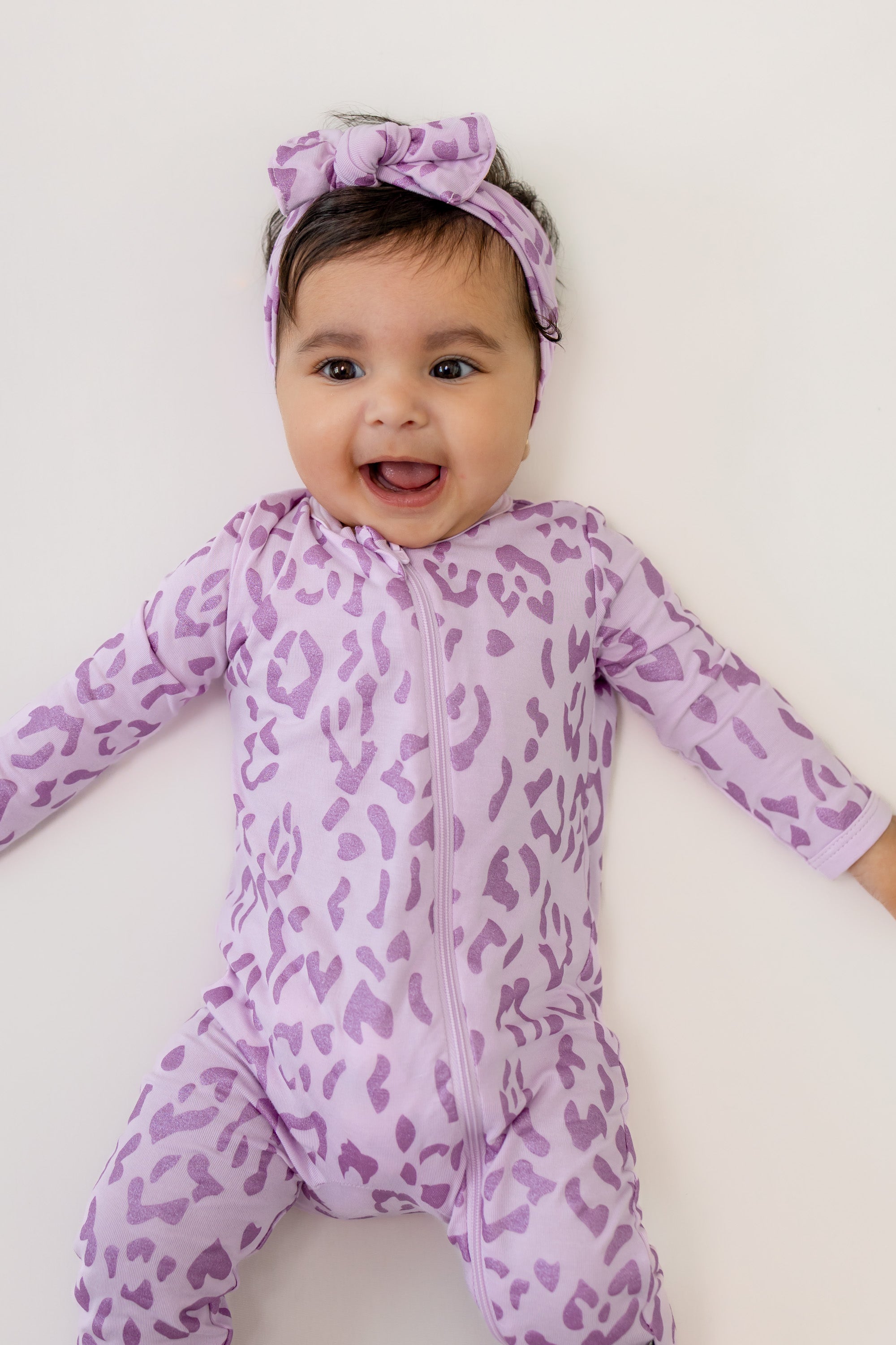 Baby wearing Thistle Leopard print zippered romper and bow headband on a beige background