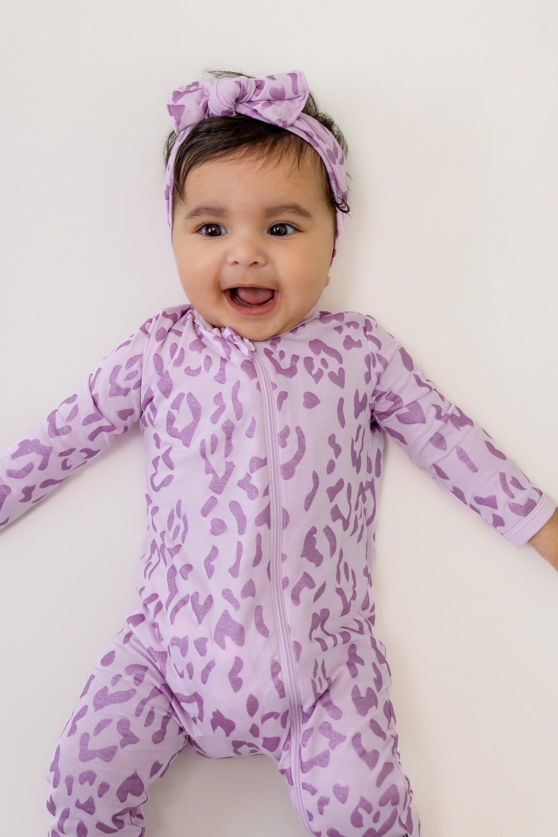 Baby wearing Thistle Leopard print zippered romper and bow headband on a beige background