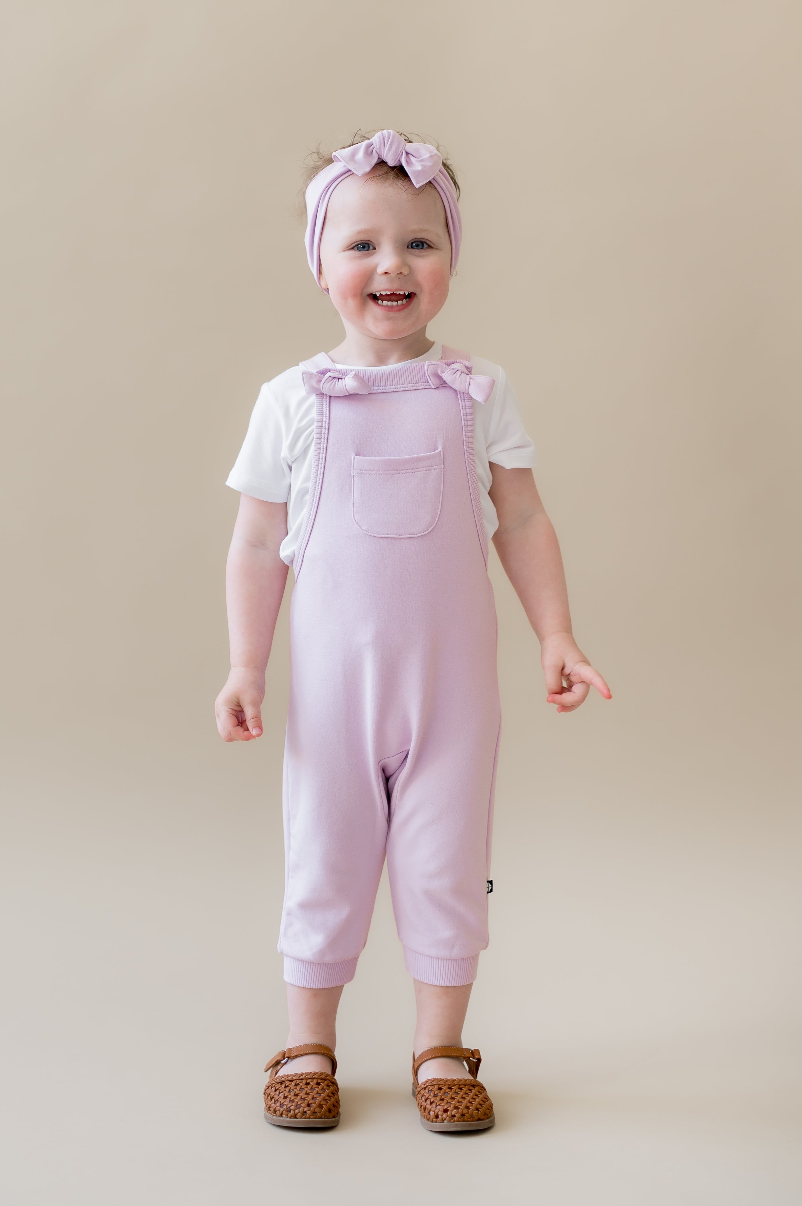 Young girl standing in front of a beige background wearing the Overall in Thistle