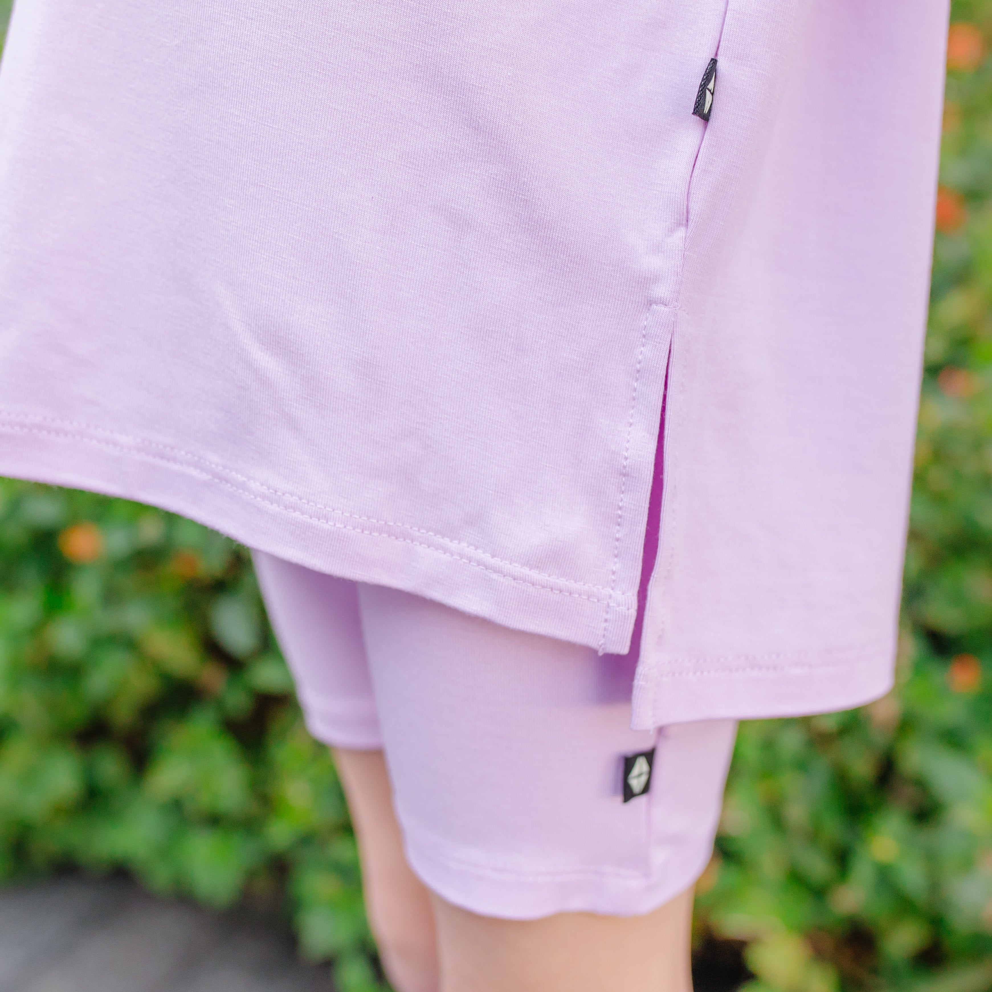 Close-up of a child wearing light purple biker shorts and oversized tee with a blurred green background