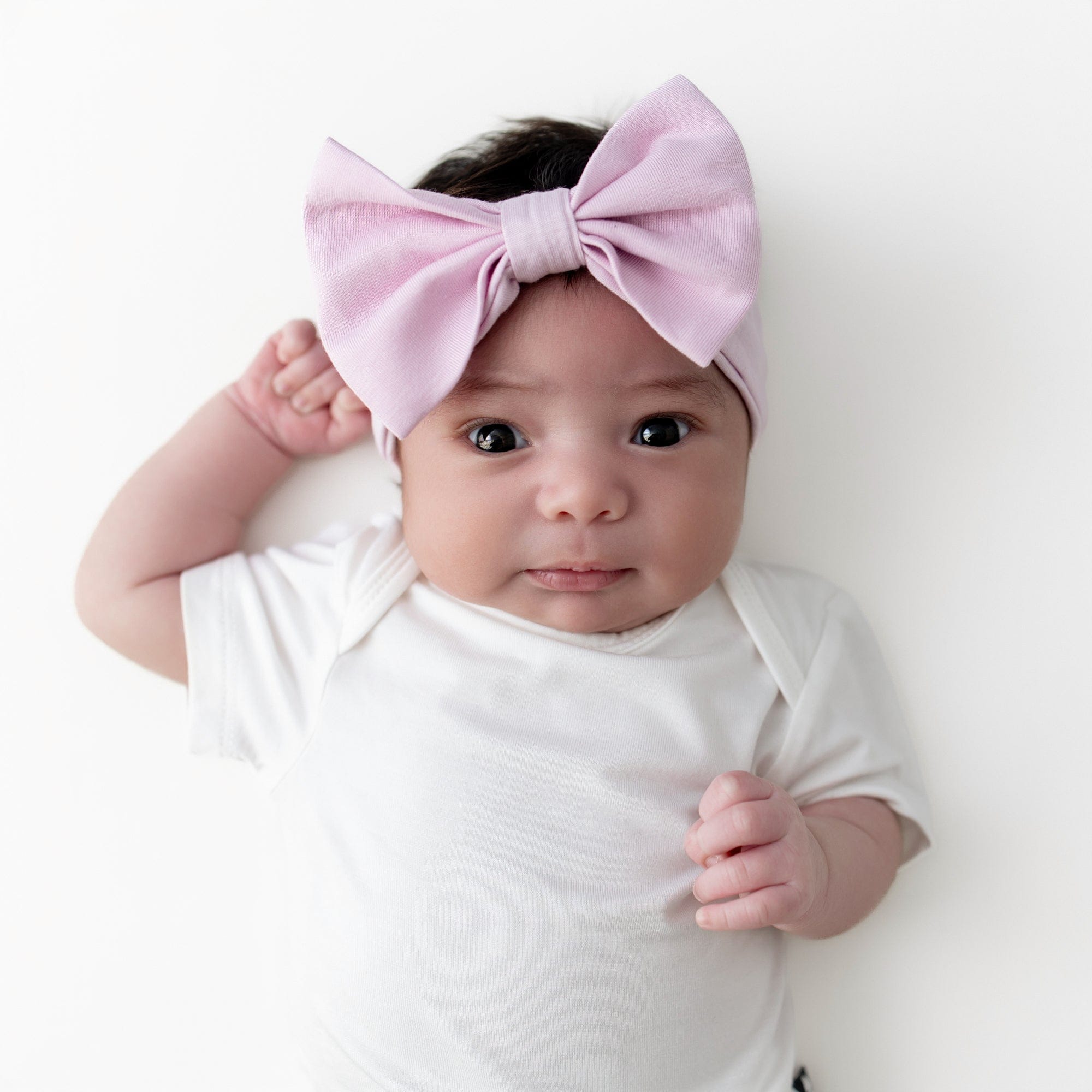 Infant girl wearing the Bow Headband in Thistle laying on a white surface