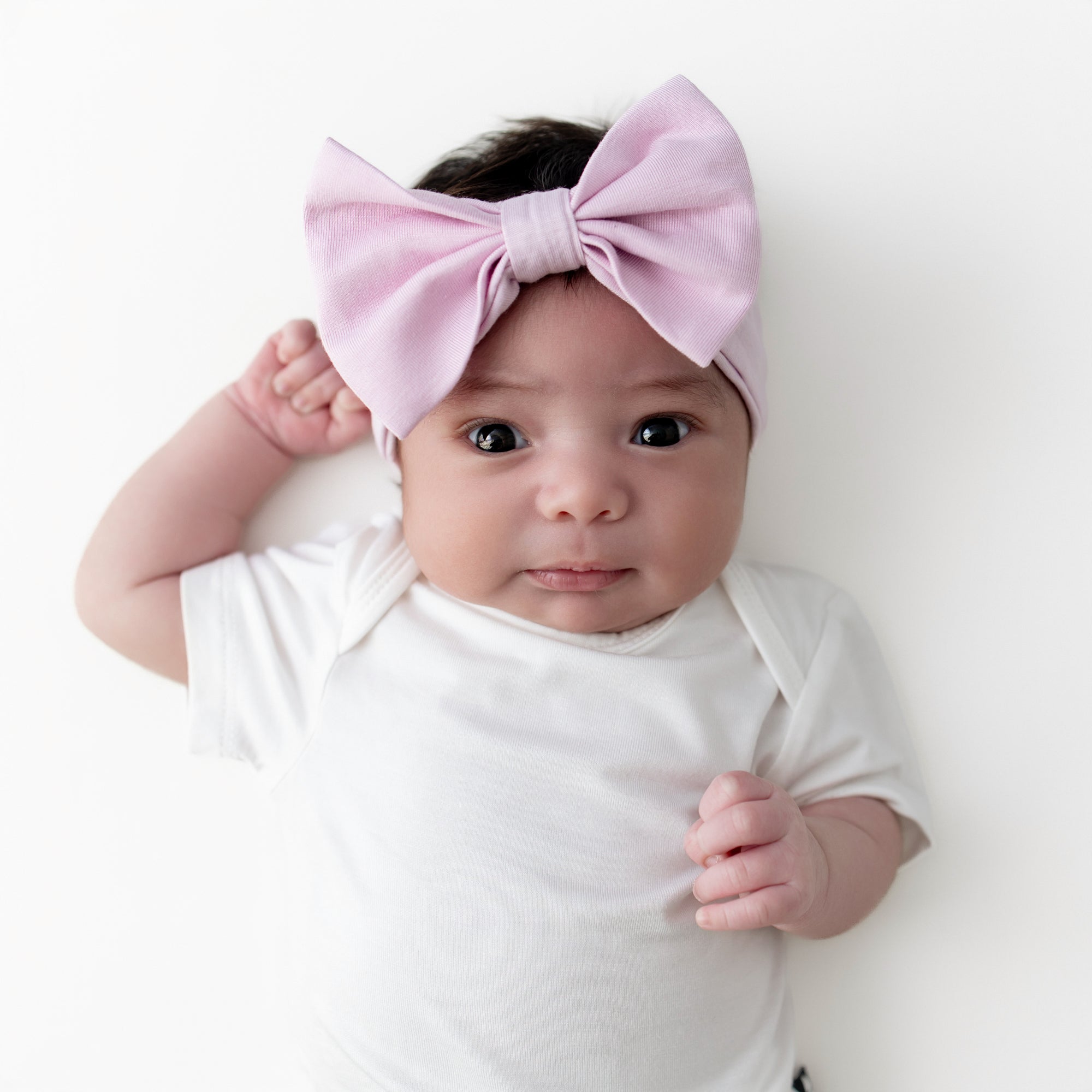 Infant girl wearing the Bow Headband in Thistle laying on a white surface