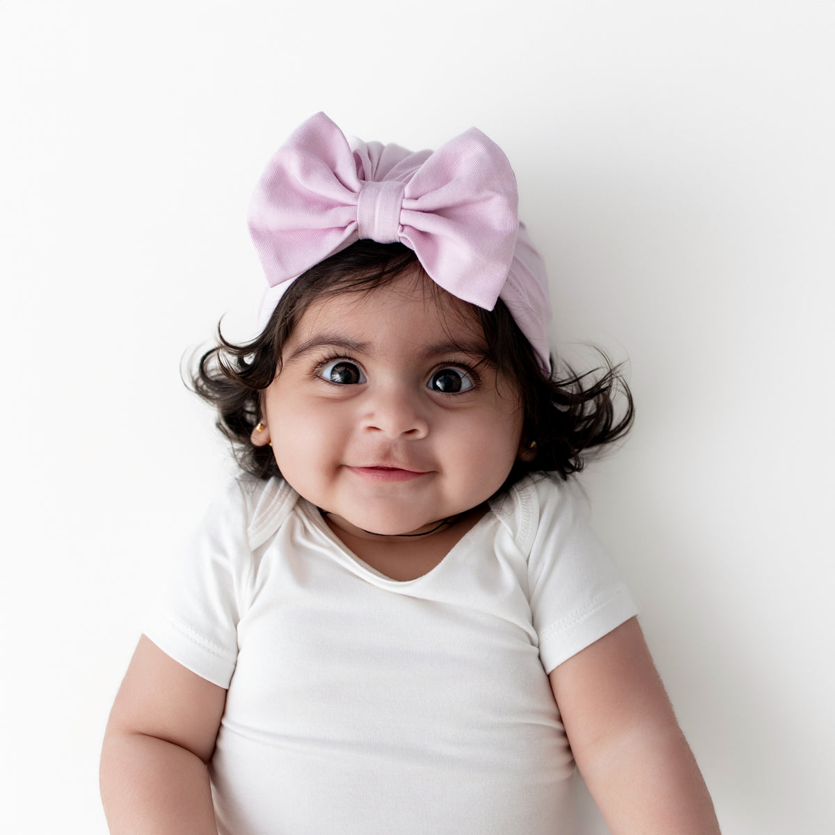 Young infant girl wearing the Bow Headwrap Thistle laying on a white surface