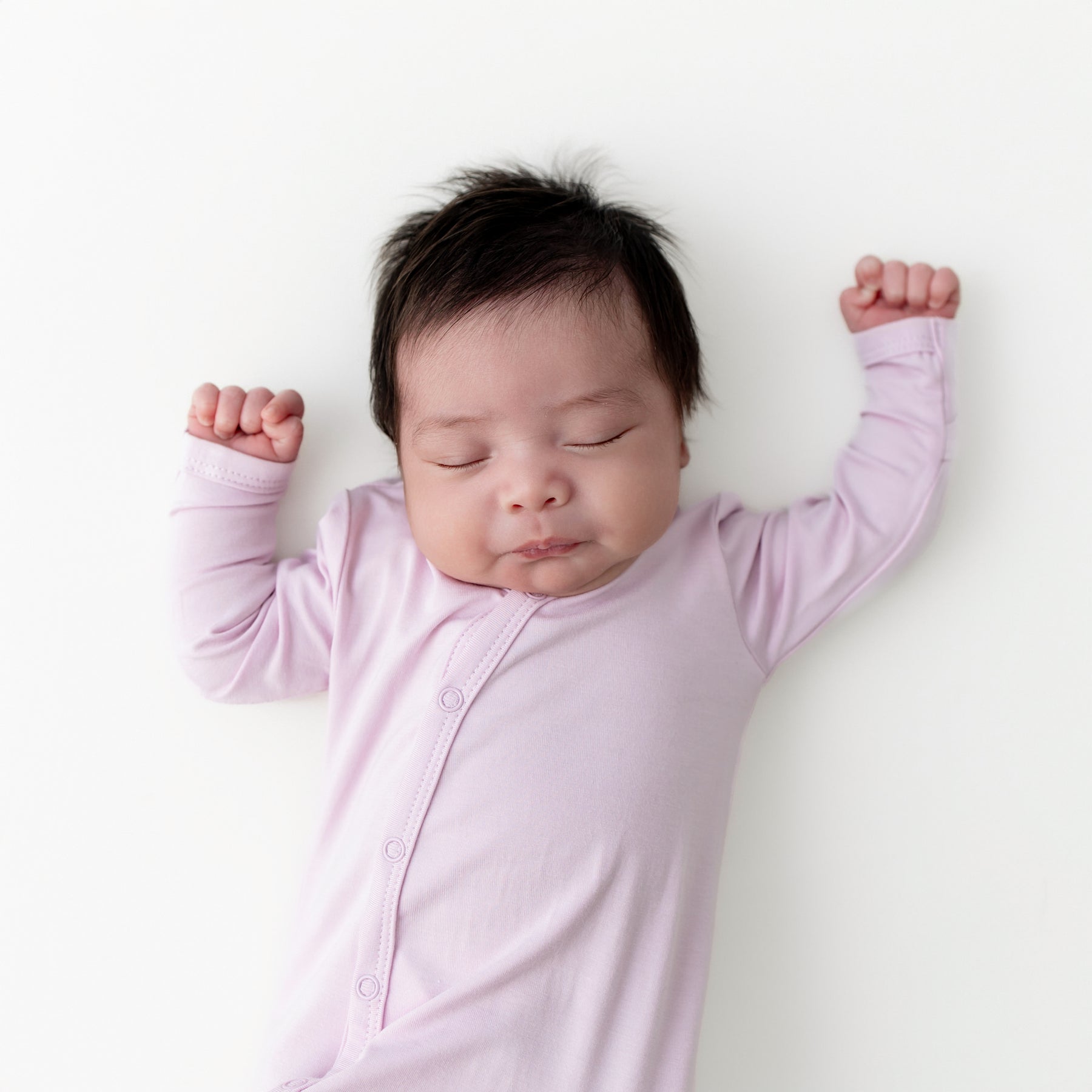 Close up of sleeping infant wearing the Bundler in Thistle laying on a white surface
