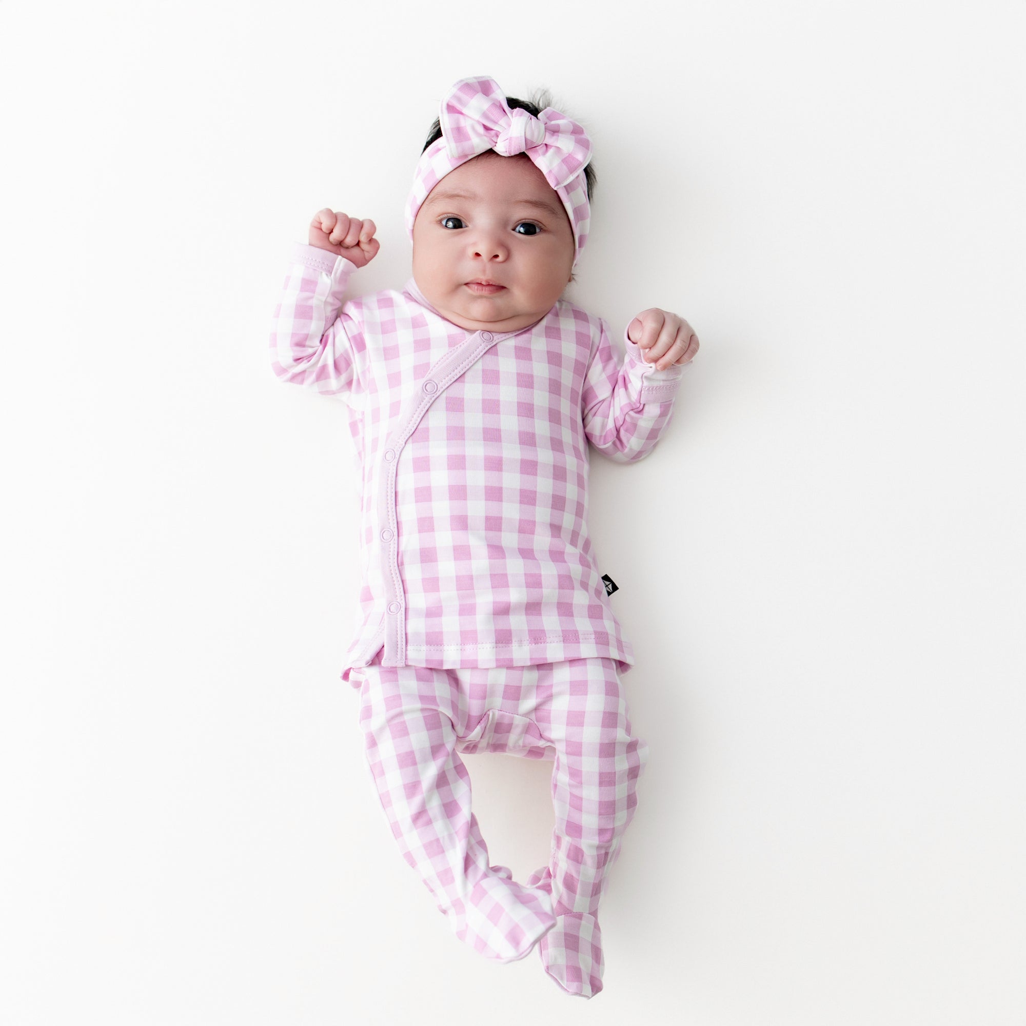 Newborn laying on a light cream surface wearing the Take Me Home Set with Bow in Gingham Thistle