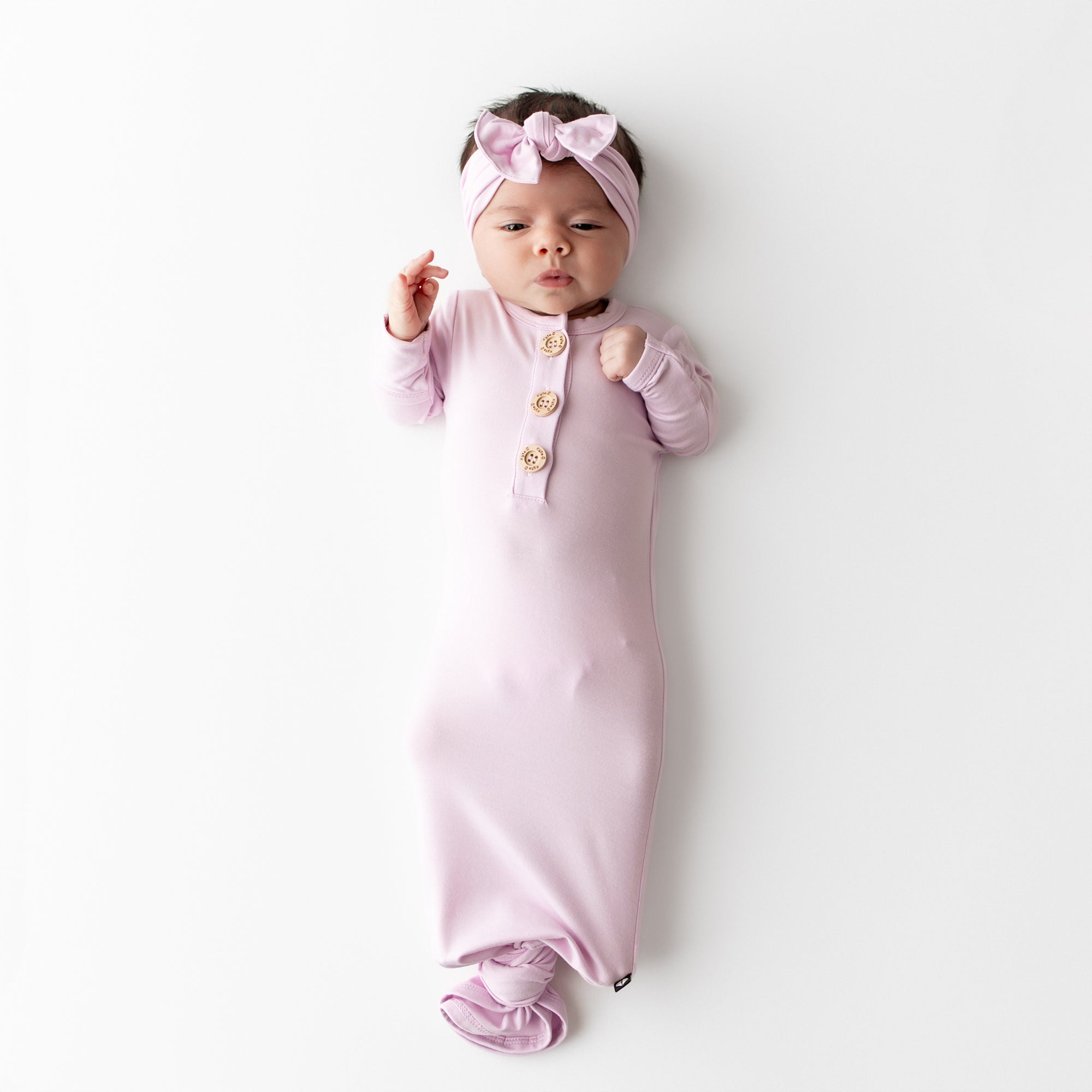 Baby wrapped in a pink knotted gown with a matching headband on a white background