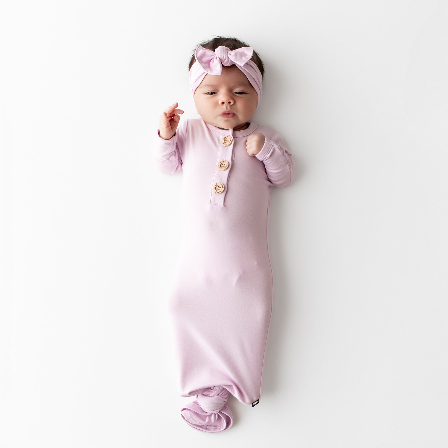 Baby wrapped in a pink knotted gown with a matching headband on a white background