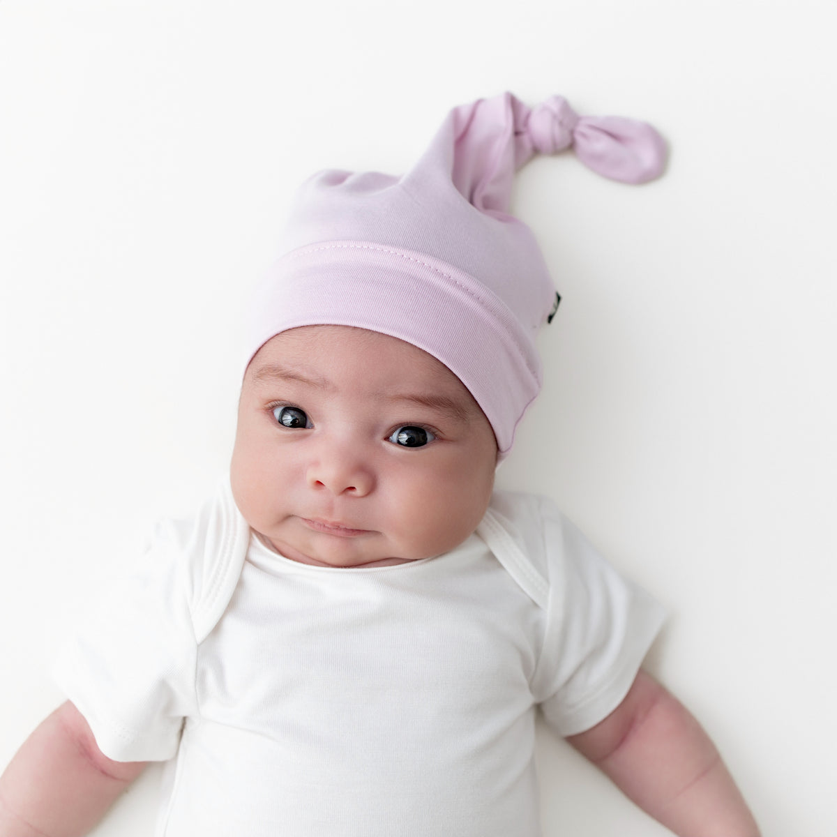 Newborn baby wearing the Knotted Cap in Thistle laying on a white surface