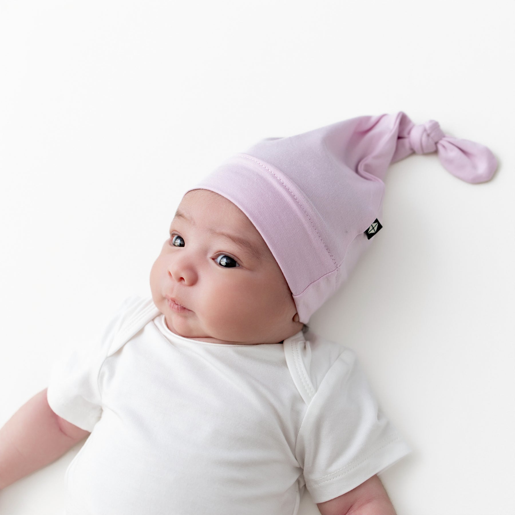 Infant girl wearing the Knotted Cap in Thistle with a white bodysuit laying on a white surface