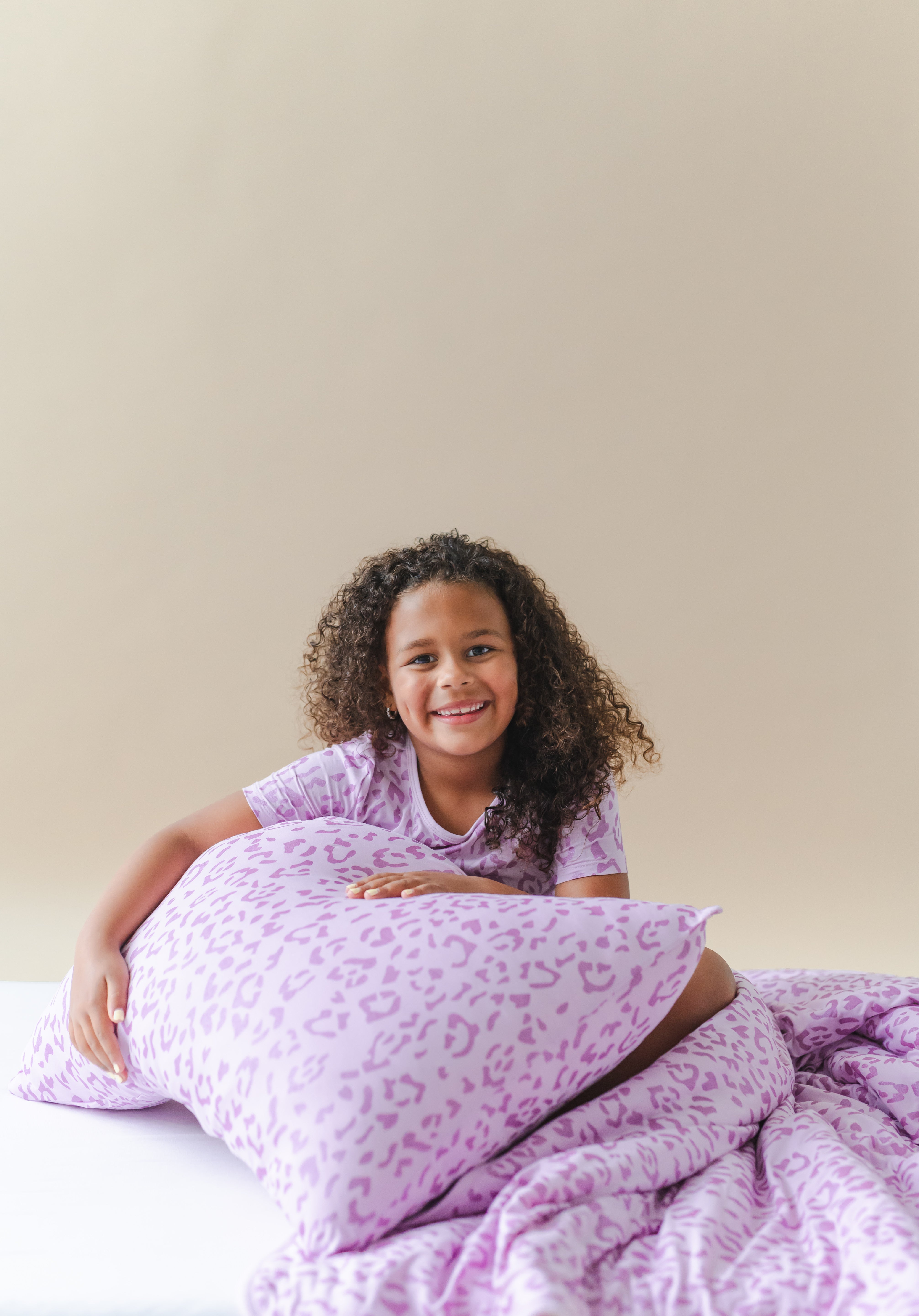 Child holding a Thistle Leopard print Standard pillowcase and blanket wearing a similar print shirt on a white sheet