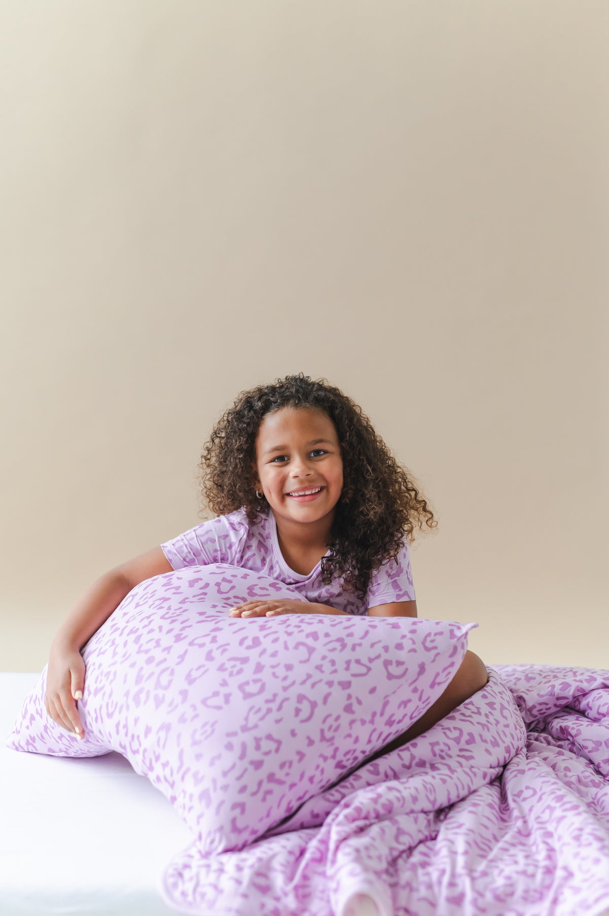 Child holding a Thistle Leopard print Standard pillowcase and blanket wearing a similar print shirt on a white sheet
