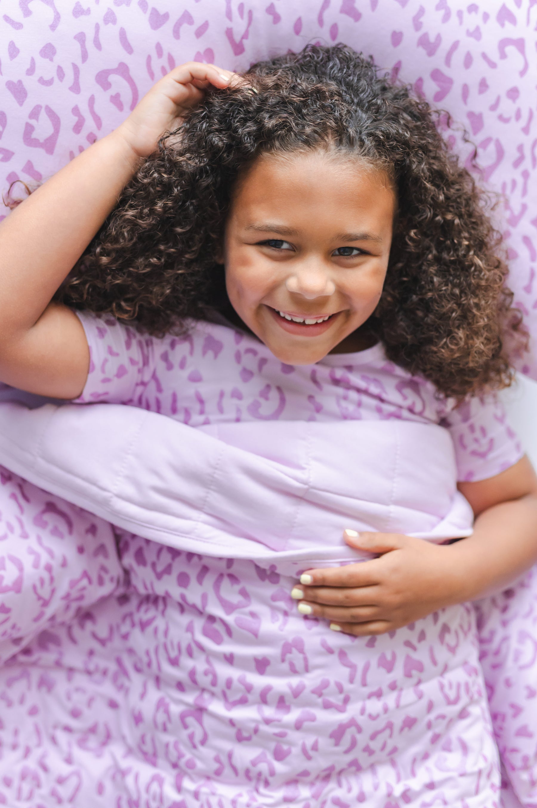 Child lying under a Thistle Leopard print Youth Blanket wearing a similar print shirt on a Thistle Leopard print pillowcase