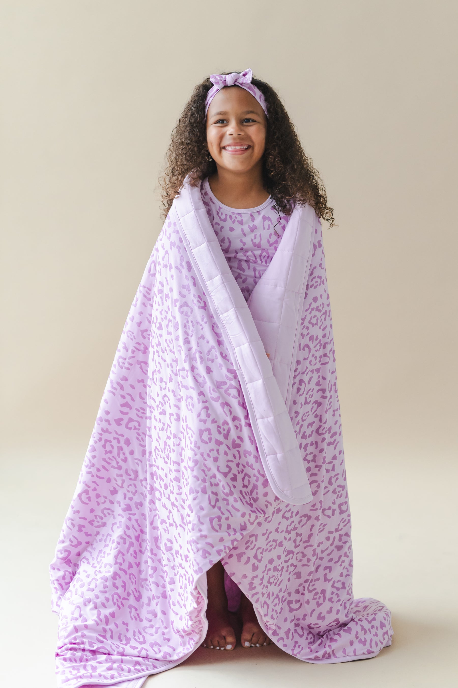 Child wrapped in Thistle Leopard print Youth Blanket wearing a similar print shirt and headband on a beige background