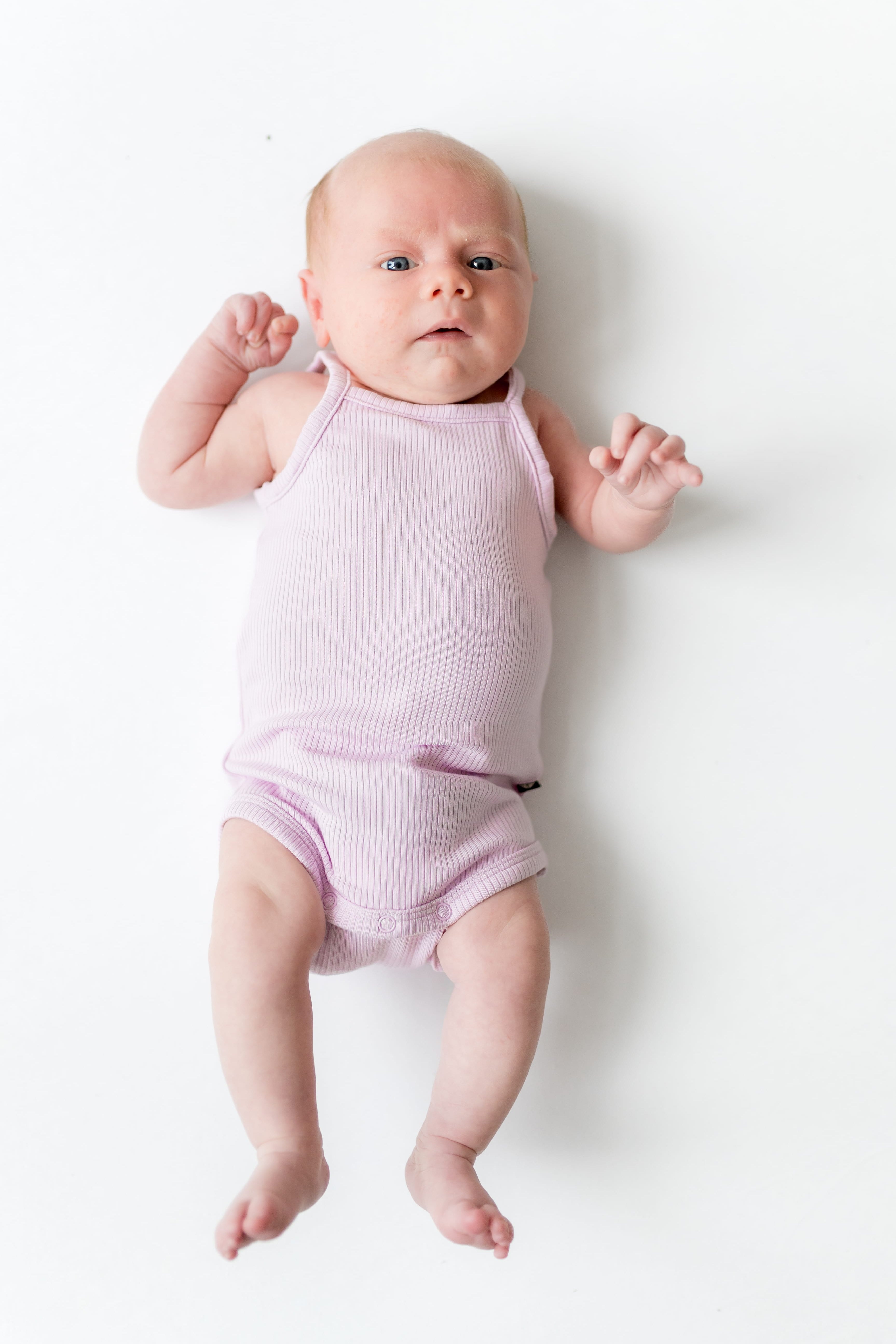 Newborn laying on a white surface wearing the Ribbed Spaghetti Strap Bodysuit in Thistle