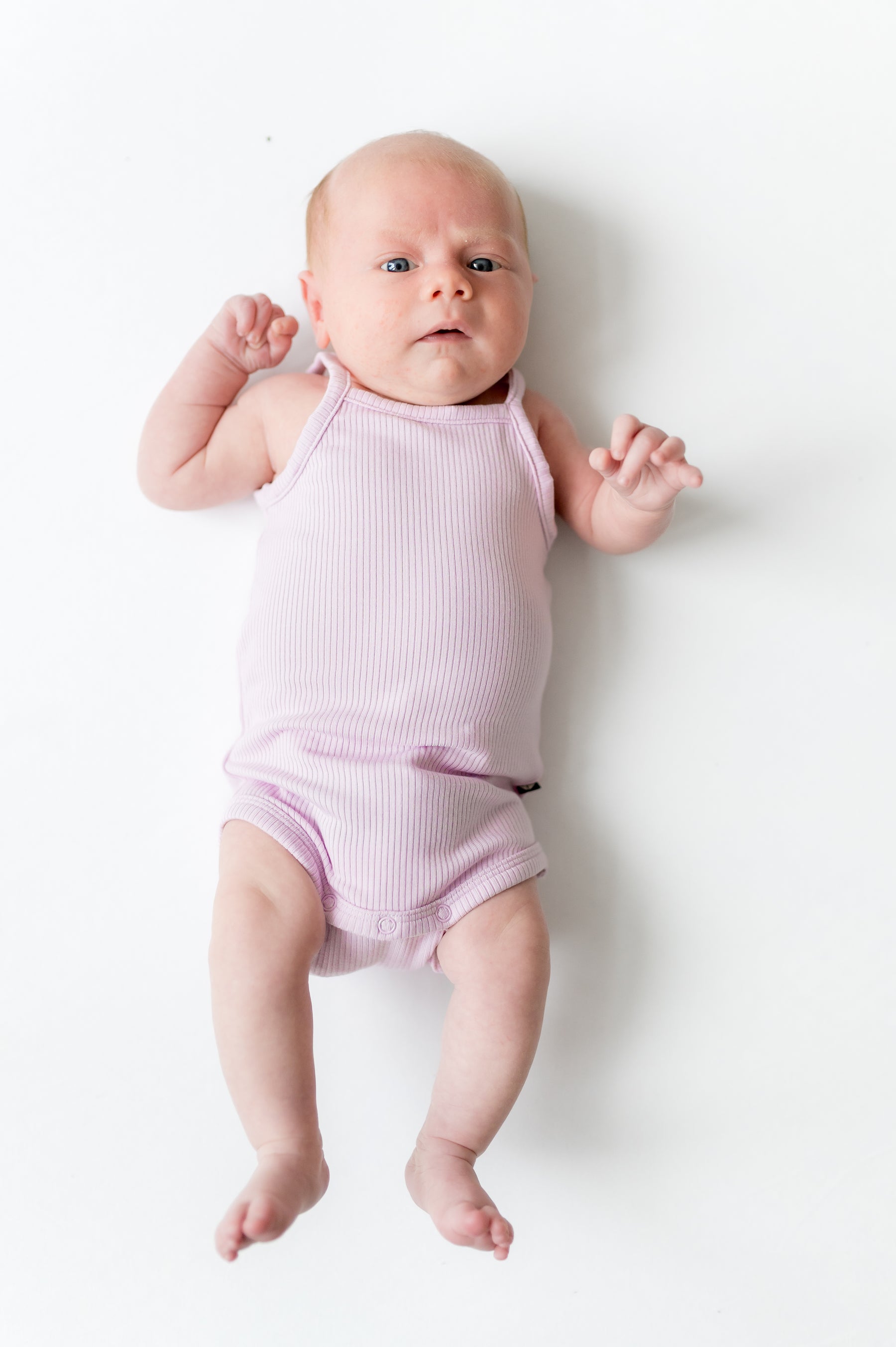 Newborn laying on a white surface wearing the Ribbed Spaghetti Strap Bodysuit in Thistle
