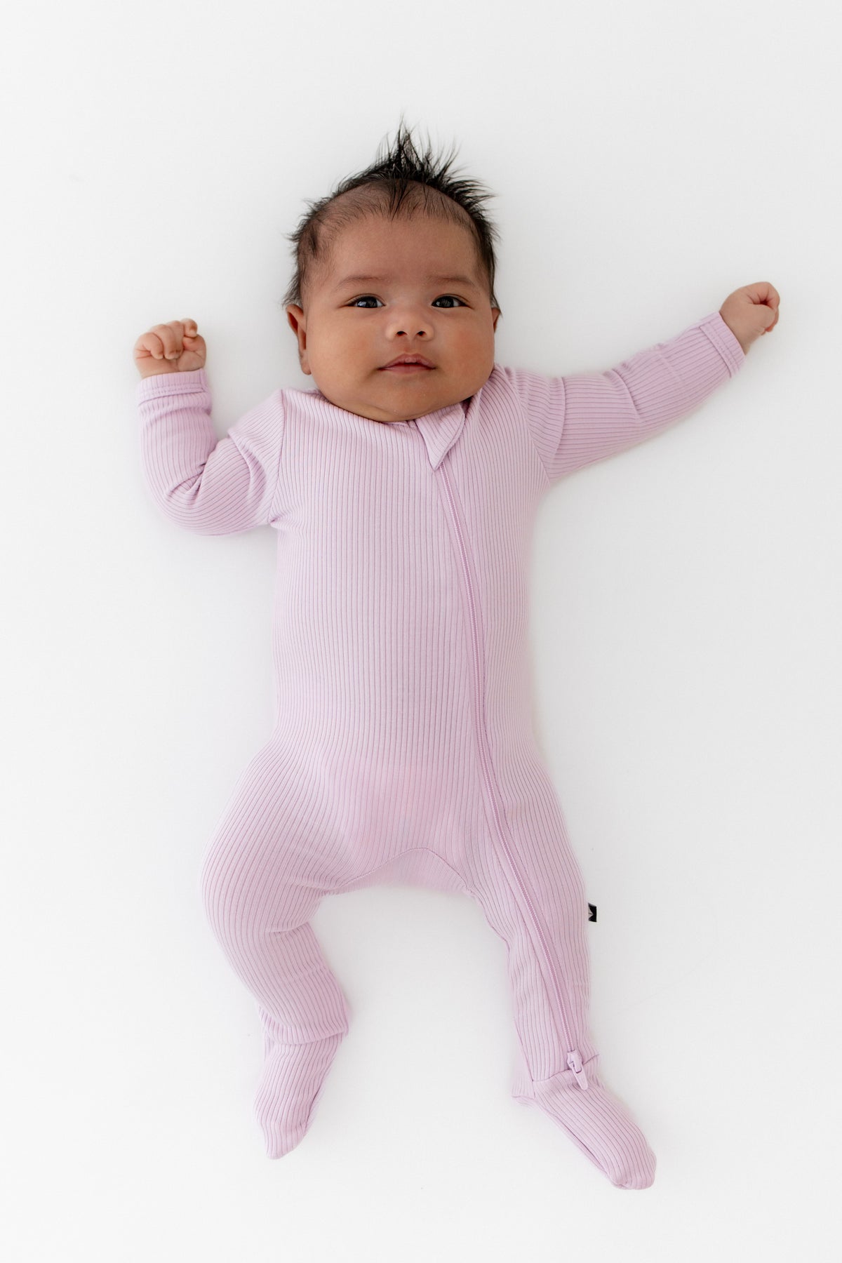 Newborn stretching wearing the Ribbed Zipper Footie in Thistle