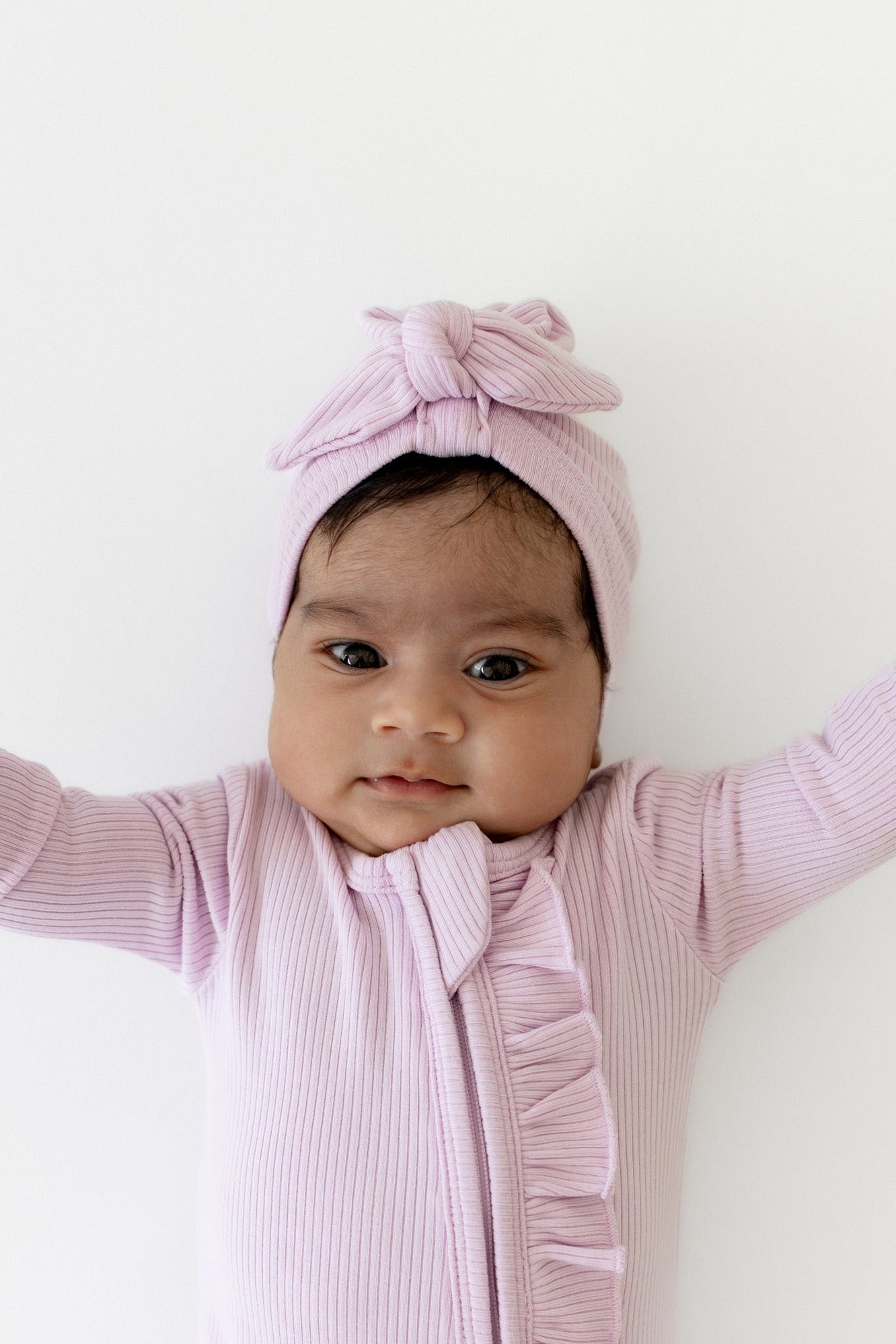 Infant wearing the Ribbed Headwrap in Thistle with matching ribbed ruffle zipper footie