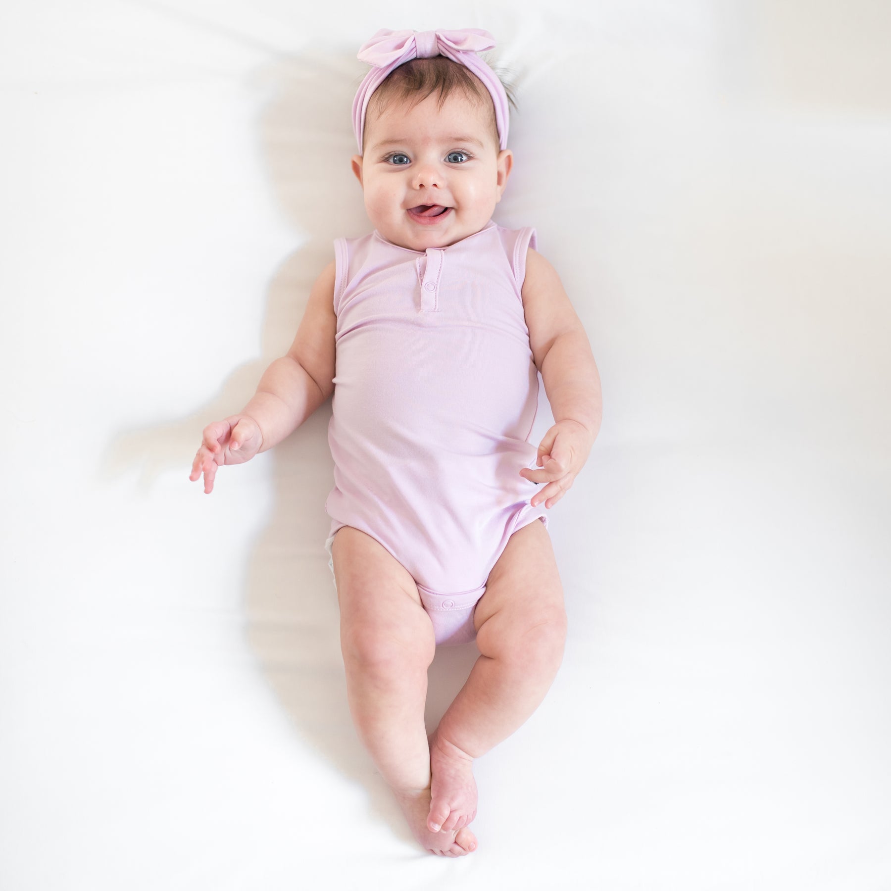 Baby wearing a sleeveless bodysuit and bow in a light purple color