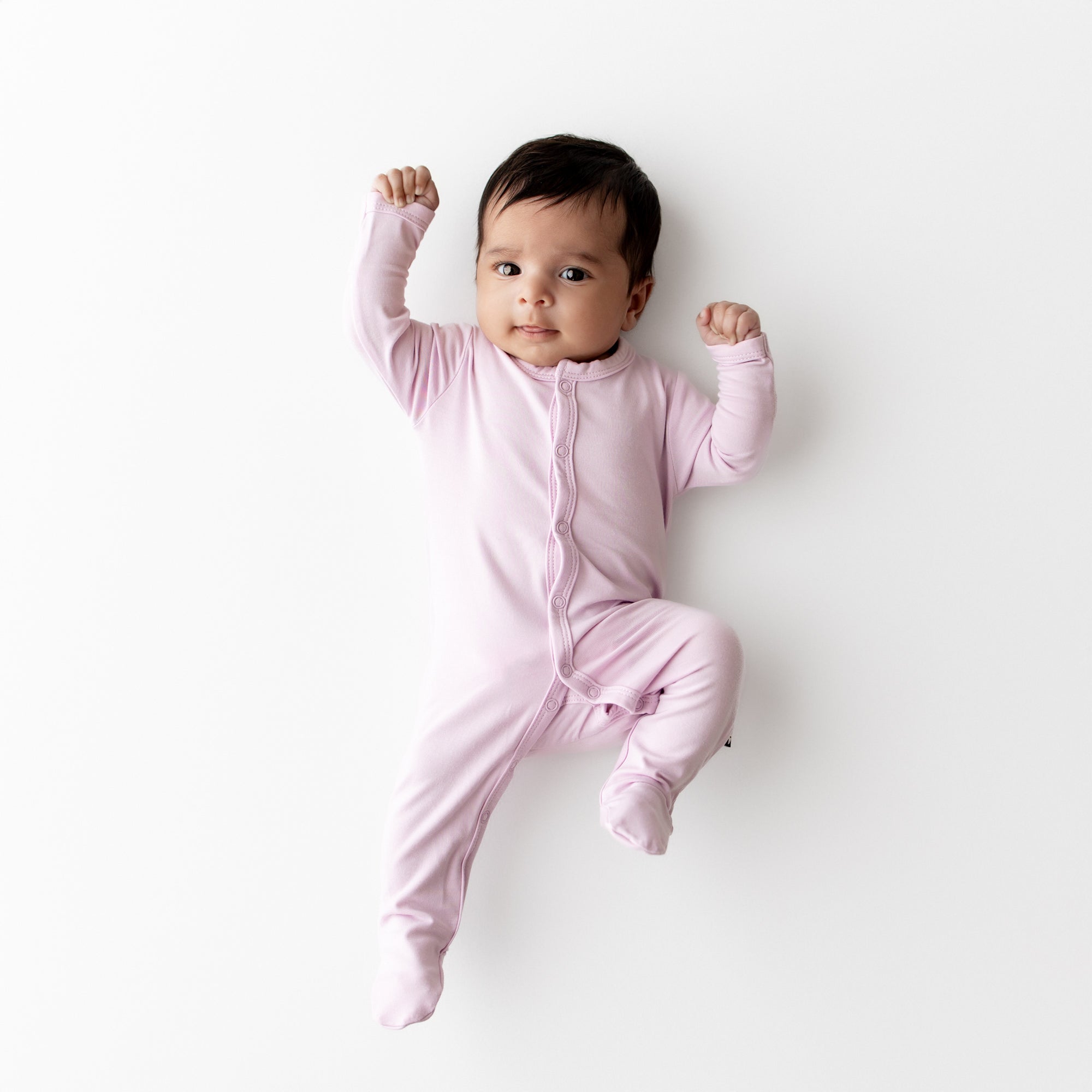 Baby in a purple snap footie lying on a white background