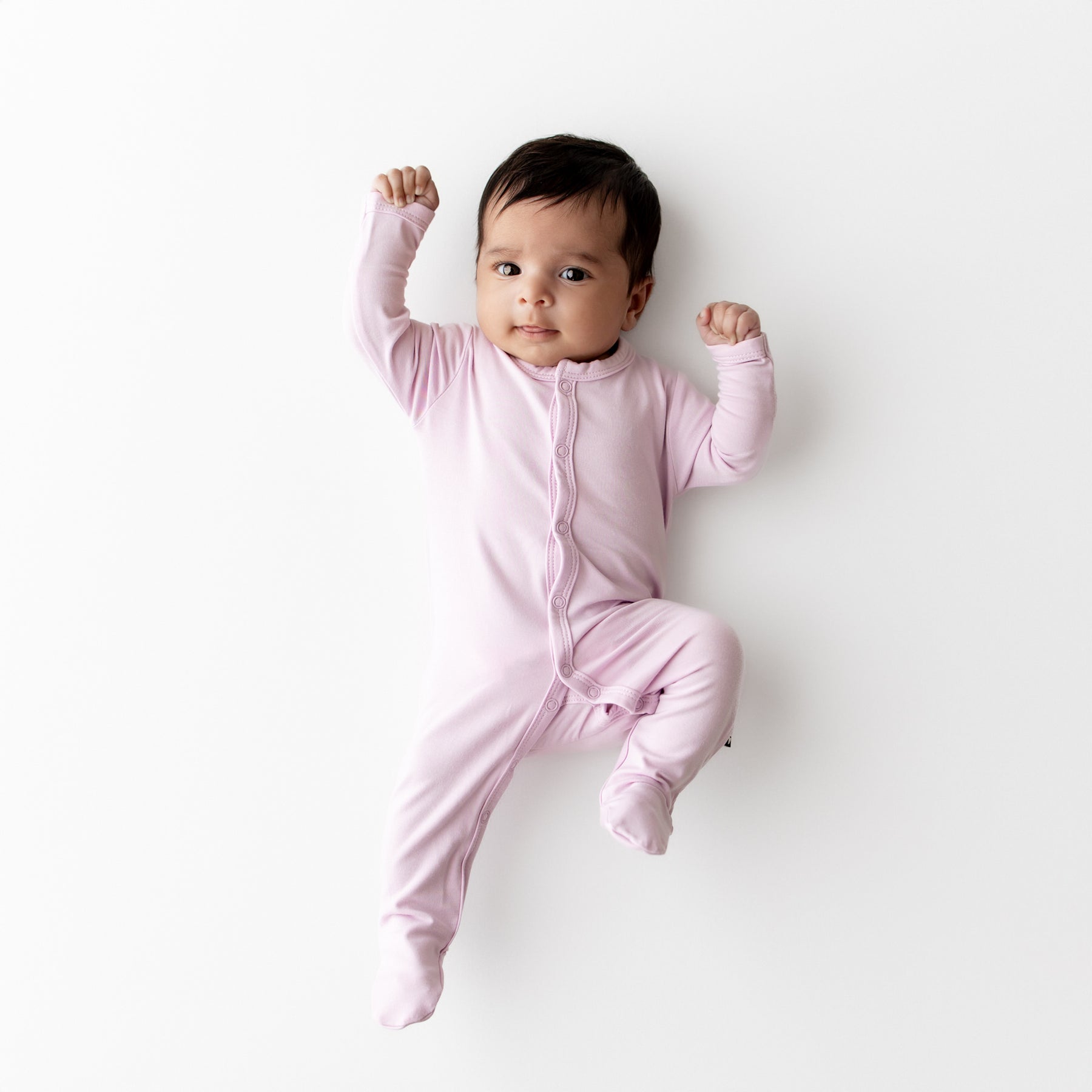 Baby in a purple snap footie lying on a white background