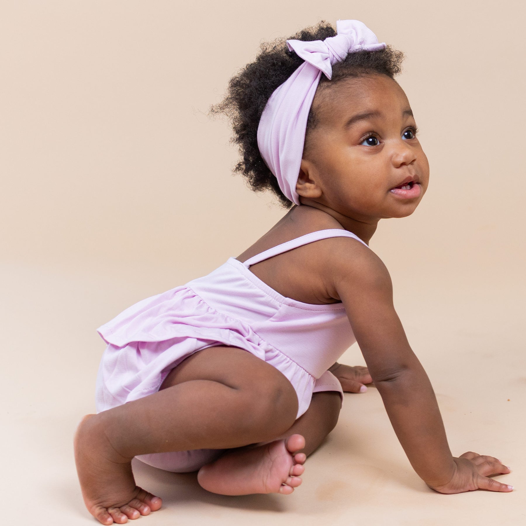 Toddler crawling on the floor wearing the Spaghetti Strap Ruffle Romper in Thistle with matching bow