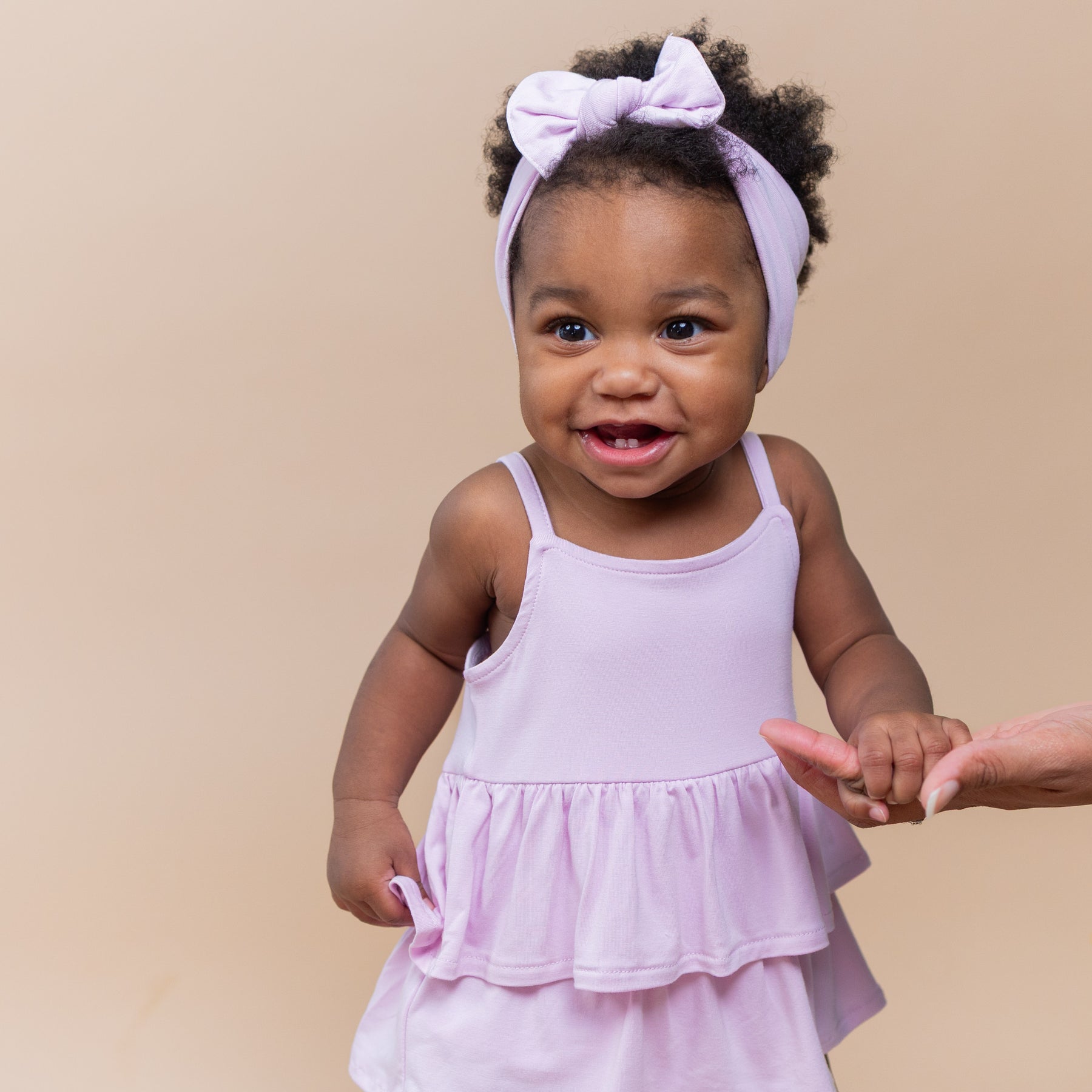 Close up of toddler model wearing the Spaghetti Strap Ruffle Romper in Thistle holding mothers hand