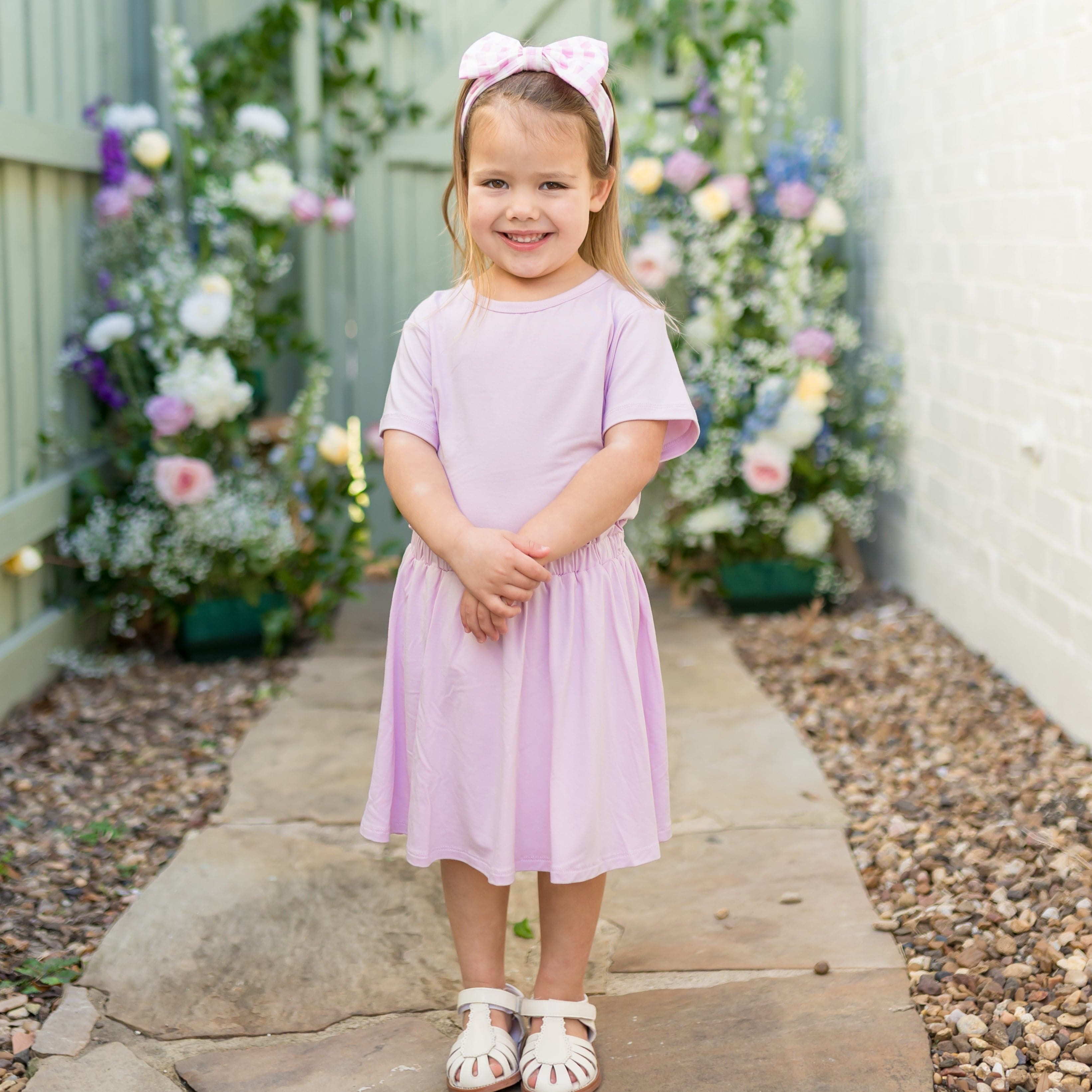 Young girl standing outside on a stone path wearing the Toddler Skort in Thistle with matching basic tee