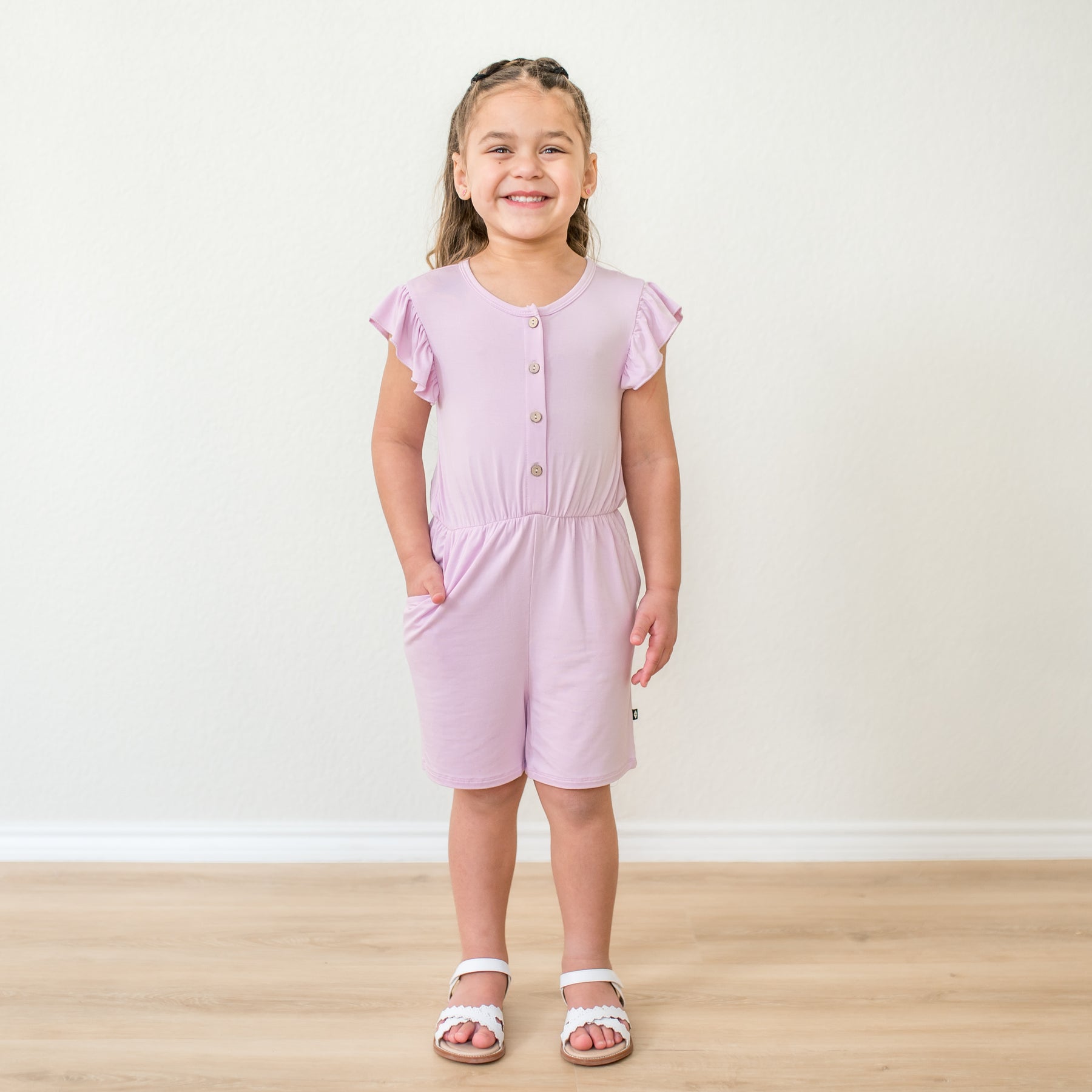 Young girl wearing a flutter sleeve romper in a light purple color