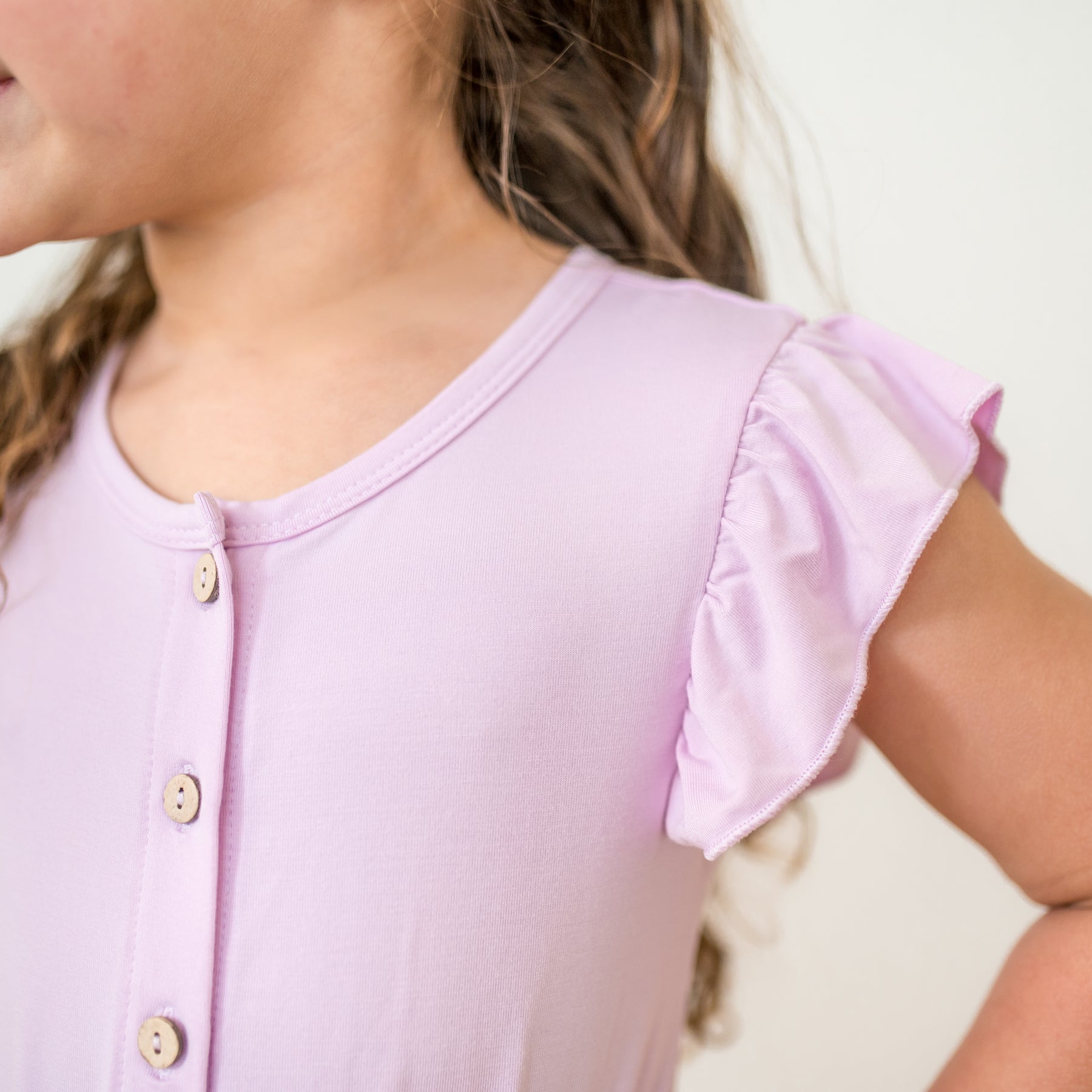 Close-up of a child wearing a light purple romper with ruffled sleeves on a neutral background