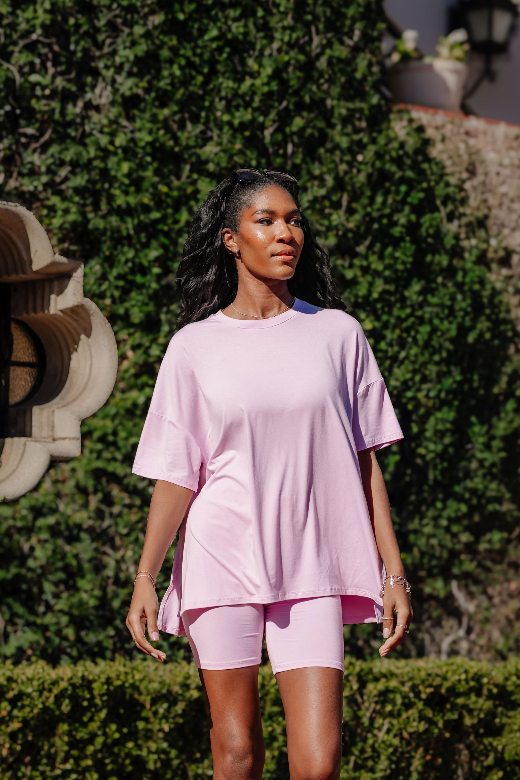 Woman wearing a purple outfit standing outdoors with greenery in the background