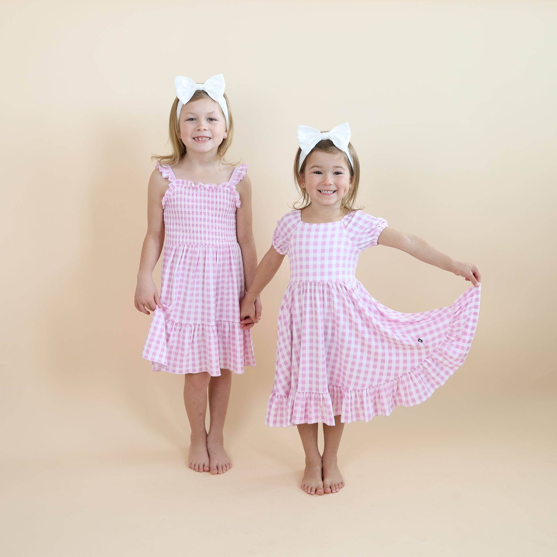 Two sisters standing side by side wearing the puff sleeve twirl dress and Smocked Dress in Gingham Thistle