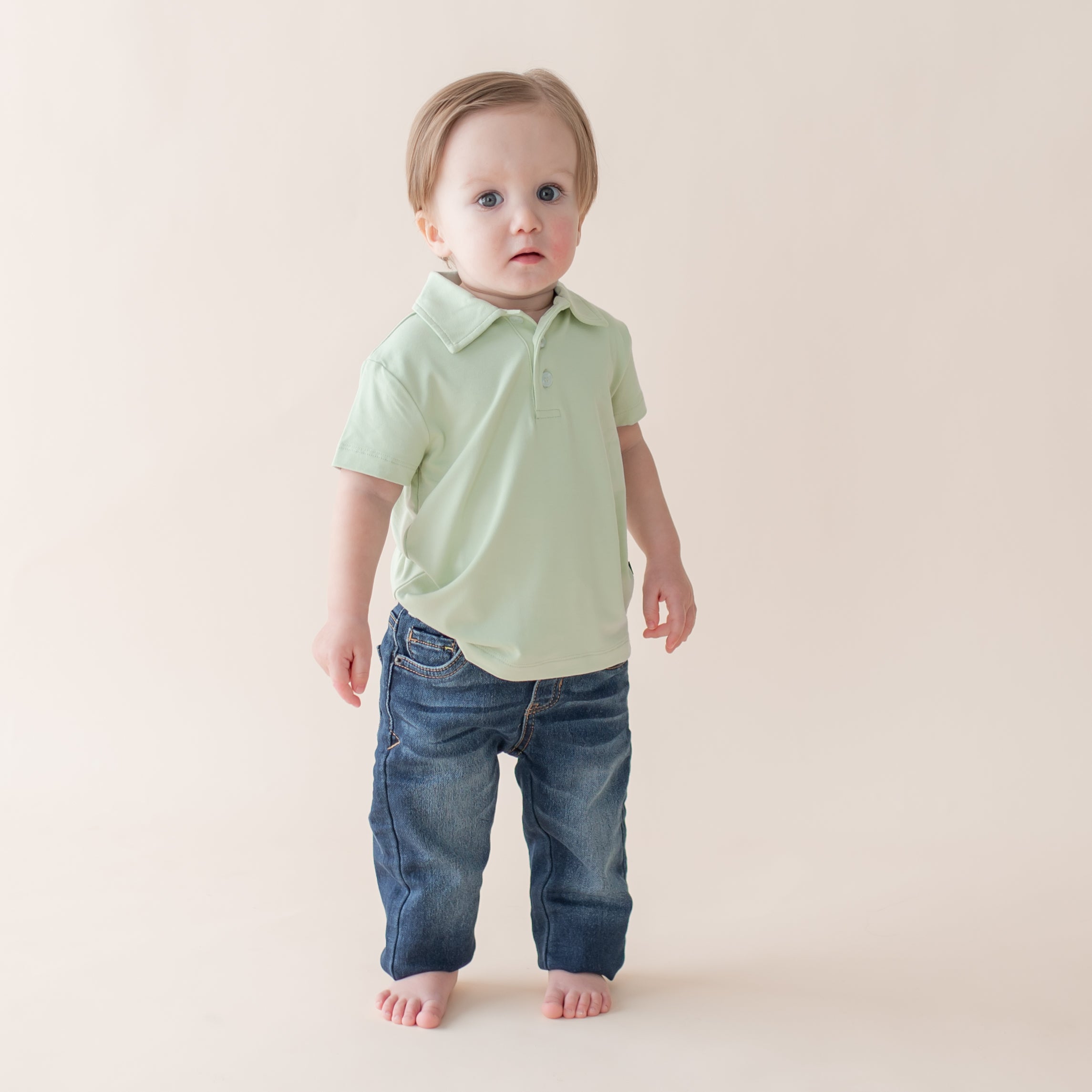 Child wearing a light green polo shirt and blue jeans on a plain background