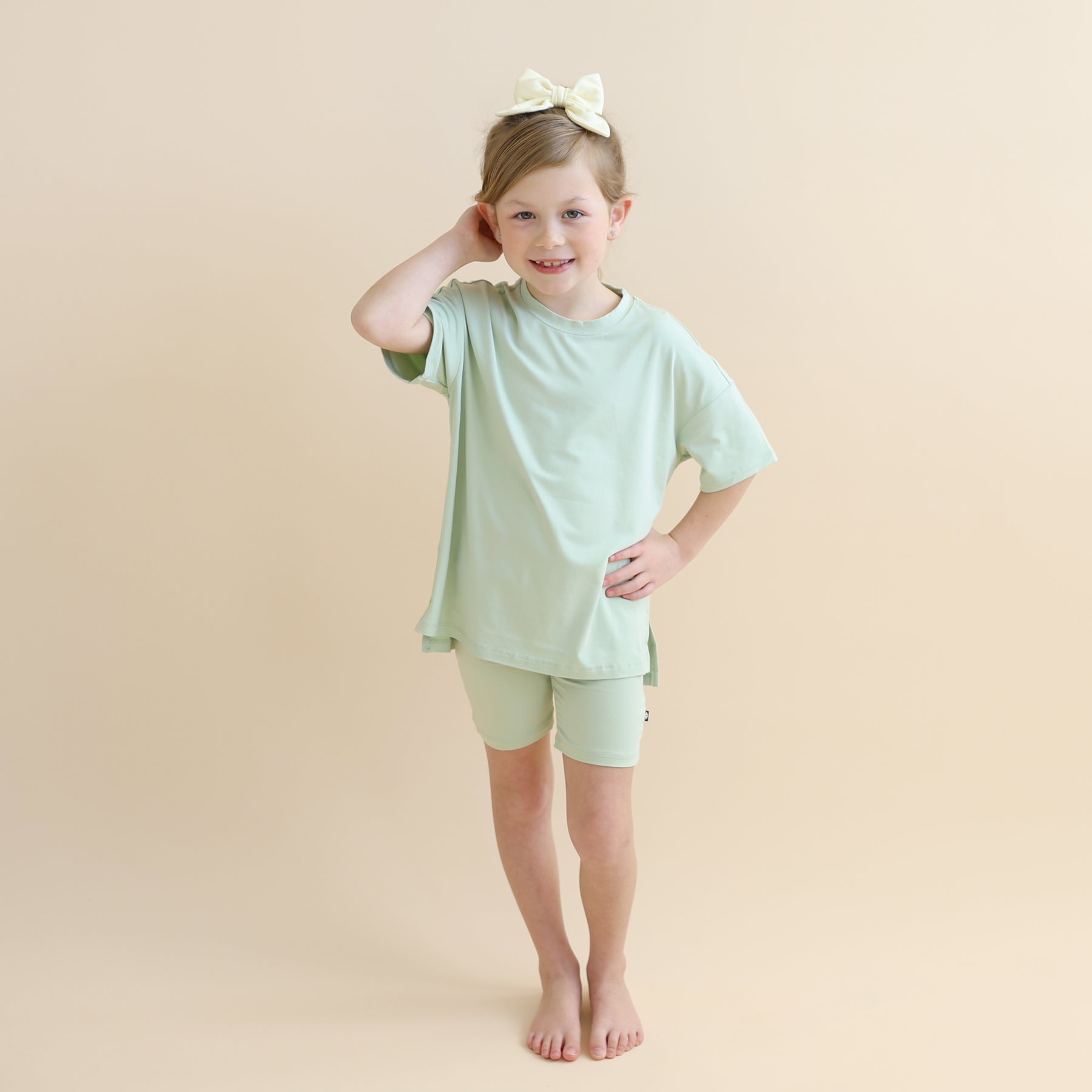 Young girl standing in front of a light neutral background wearing the Toddler Biker Short Set in Basil