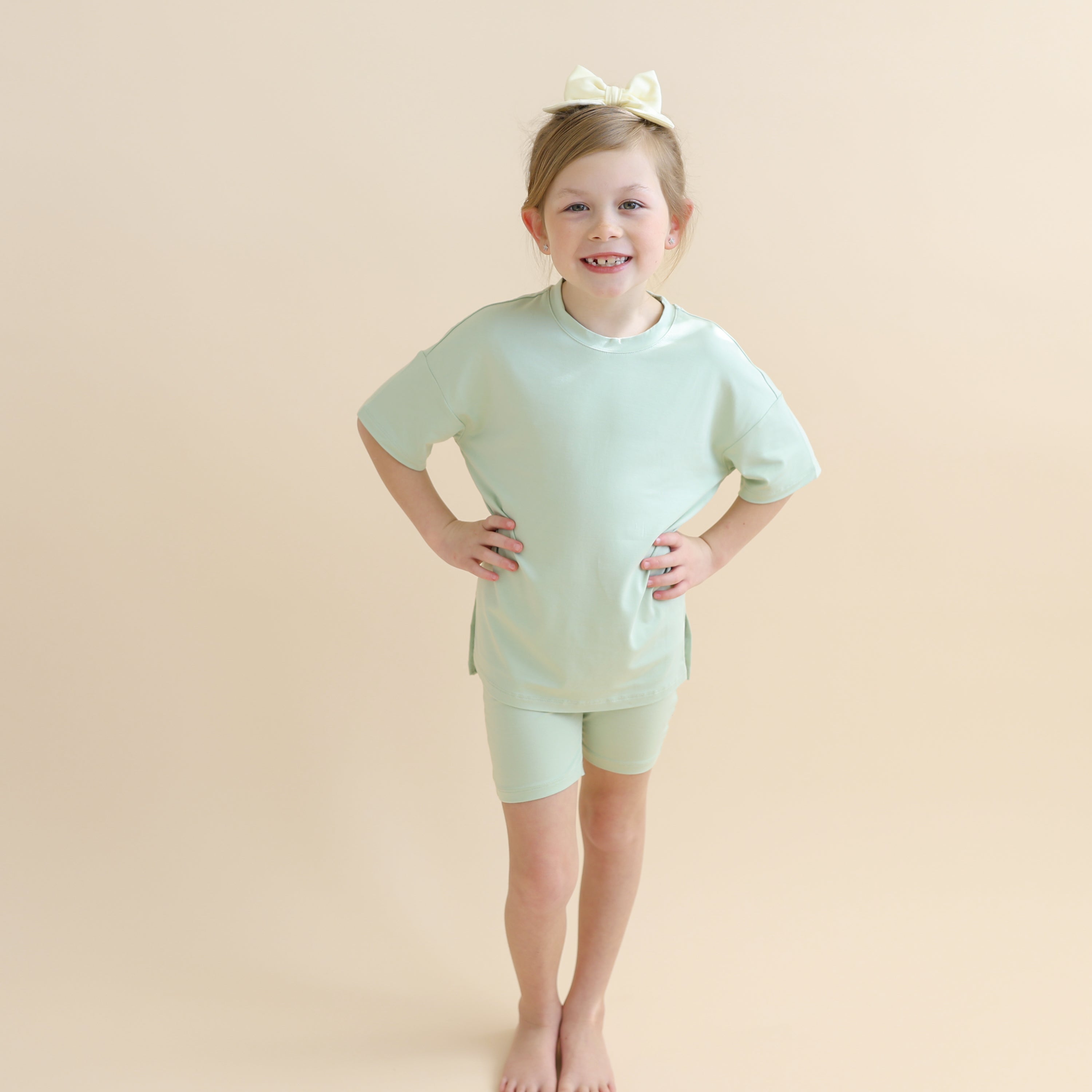 Young girl wearing the Toddler Biker Short Set in Basil standing in front of a taupe background