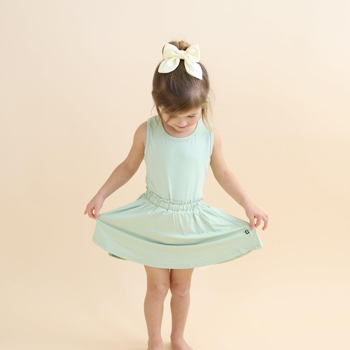 Young girl wearing the Toddler Skort in Basil holding the hem out paired with matching tank top