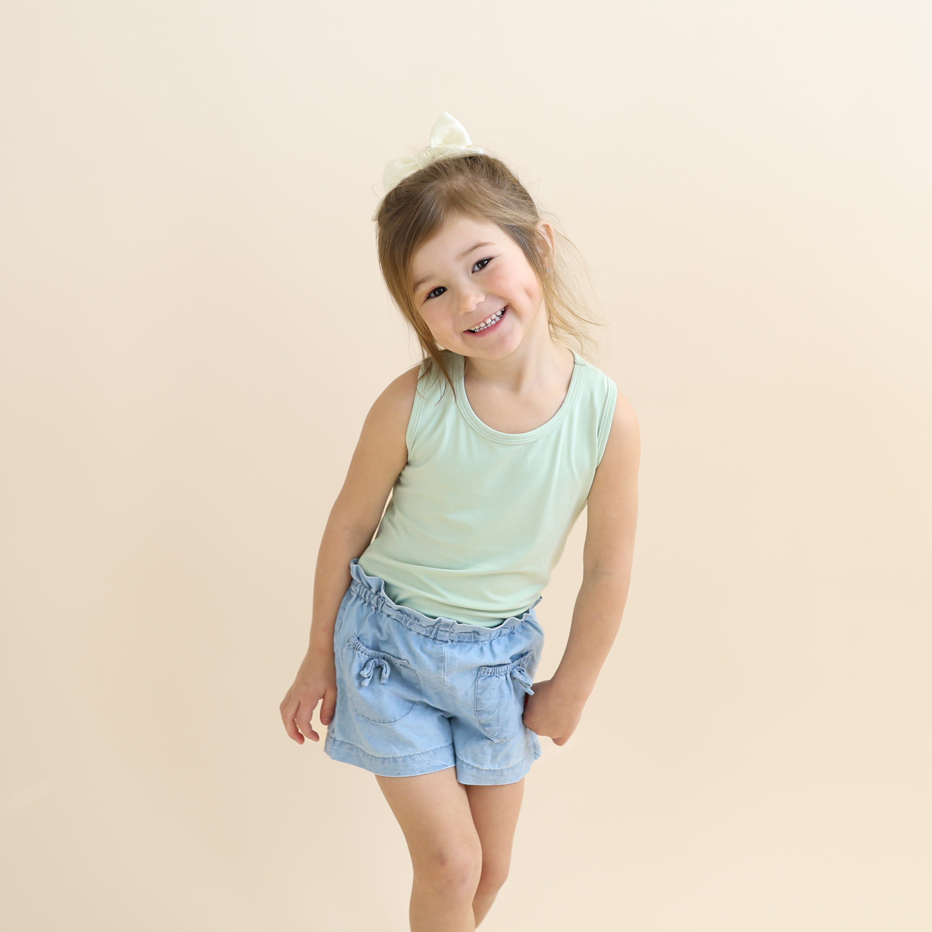 Young girl posing wearing the Toddler Tank Top in Basil with jean shorts